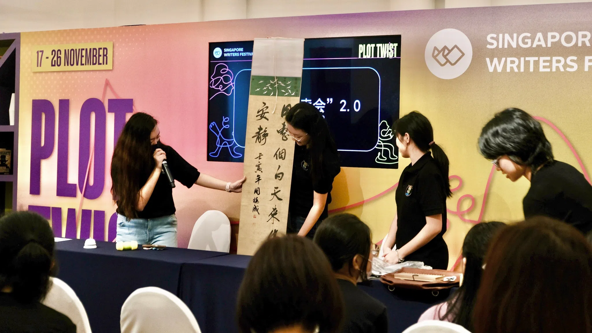 主持人周佳铃（左一）为大家介绍由本地书法家周德成捐赠的书法作品。（张菲扬摄）