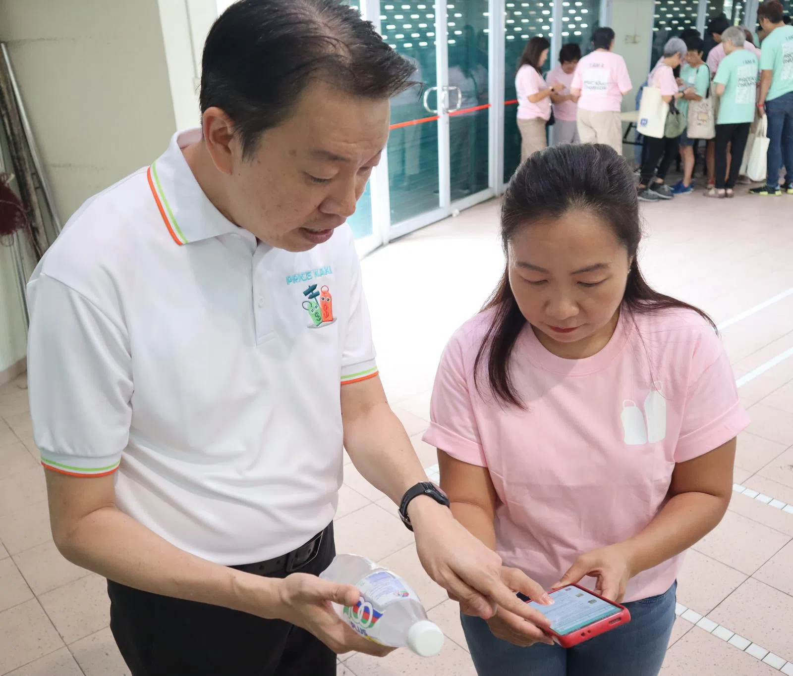 新加坡消费者协会会长杨益财（左）和“省钱达人”社区志愿者杨珊凤分享如何使用Price Kaki应用，查找和比较饮料的价格。（新加坡消费者协会提供）
