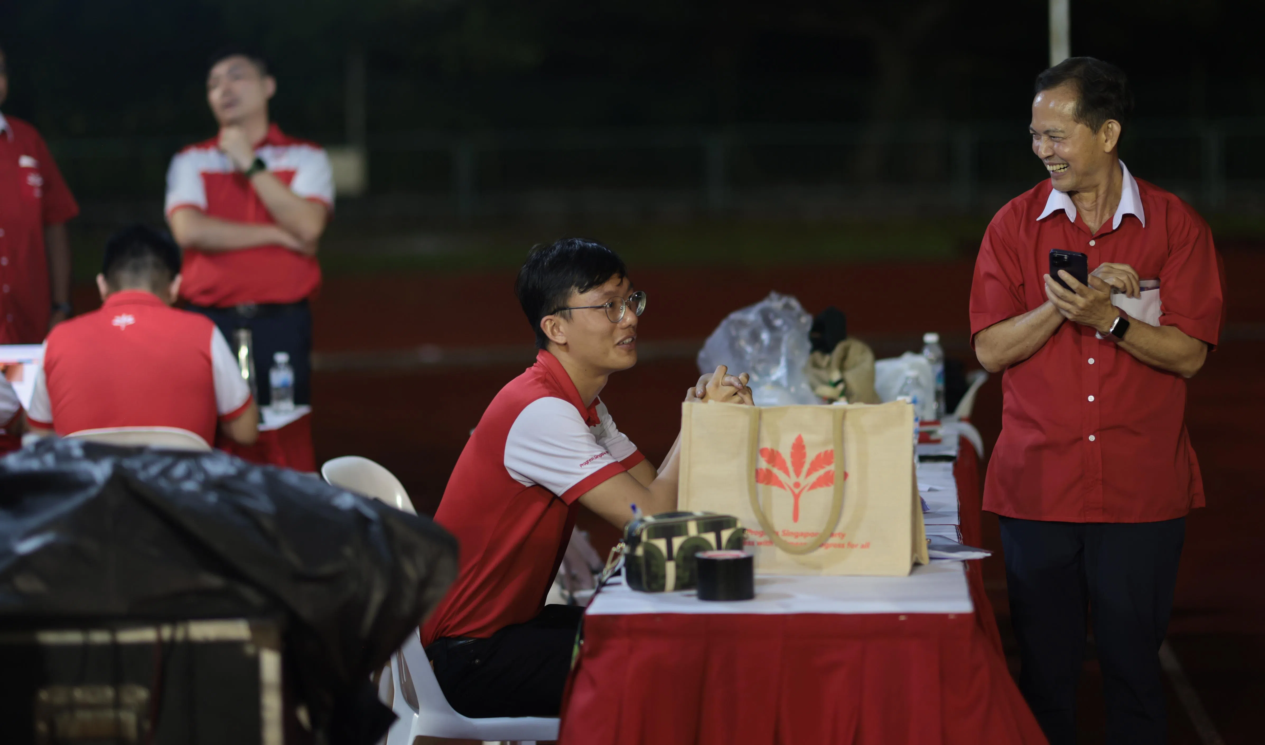 新加坡前进党4月26日在武吉甘柏体育场举行群众大会。前进党秘书长梁文辉（右一）在台下与党工轻松交谈。（李冠卫摄）