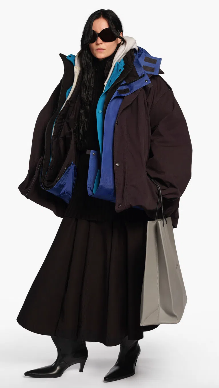 颠纳2026年春夏成衣系列放大、夸大服装的轮廓、形体，注意模特儿手拿的不是普通的“购物纸袋”而是像纸袋的矜贵皮袋。（取自品牌网站）