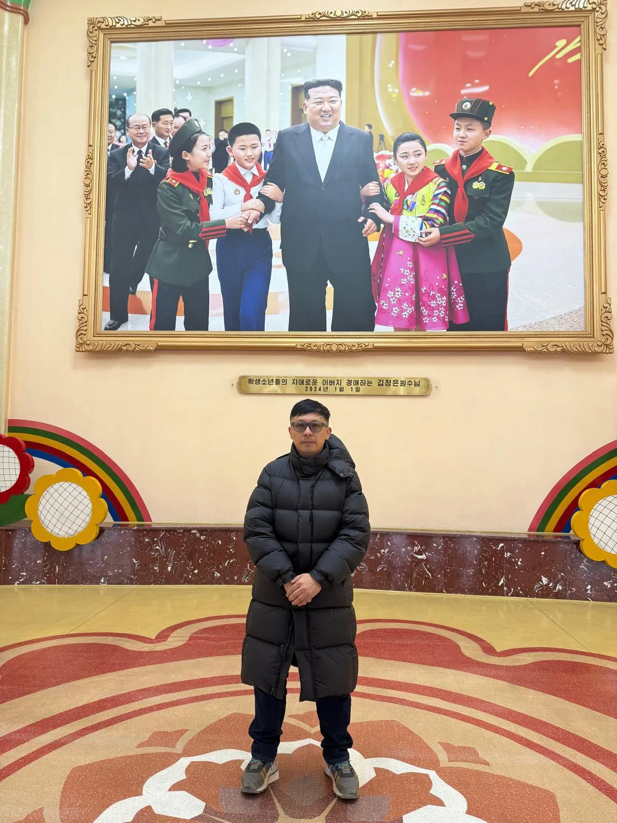 刘保罗在一副朝鲜最高领袖金正恩与孩童合照的巨型照片前留影。 （受访者提供）
