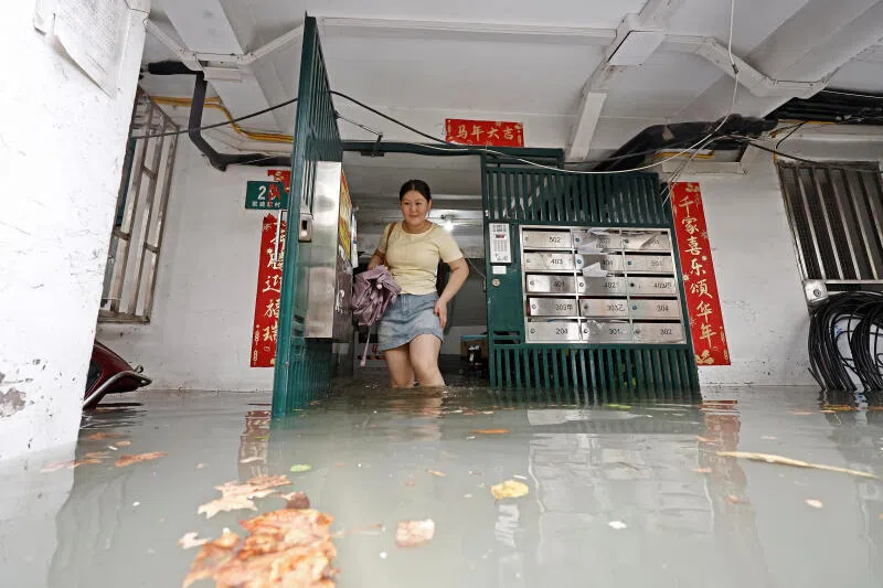 随着台风“白海豚”逼近上海，当地遭遇强降雨，一个住宅小区出现积水，一名穿着短裙的居民涉水而行。（路透社）
