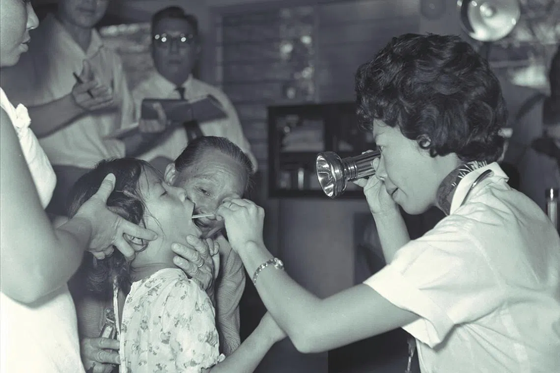 60年代的中央医院，医疗人员手拿电筒，蹲下为小病患进行检查。（档案照）