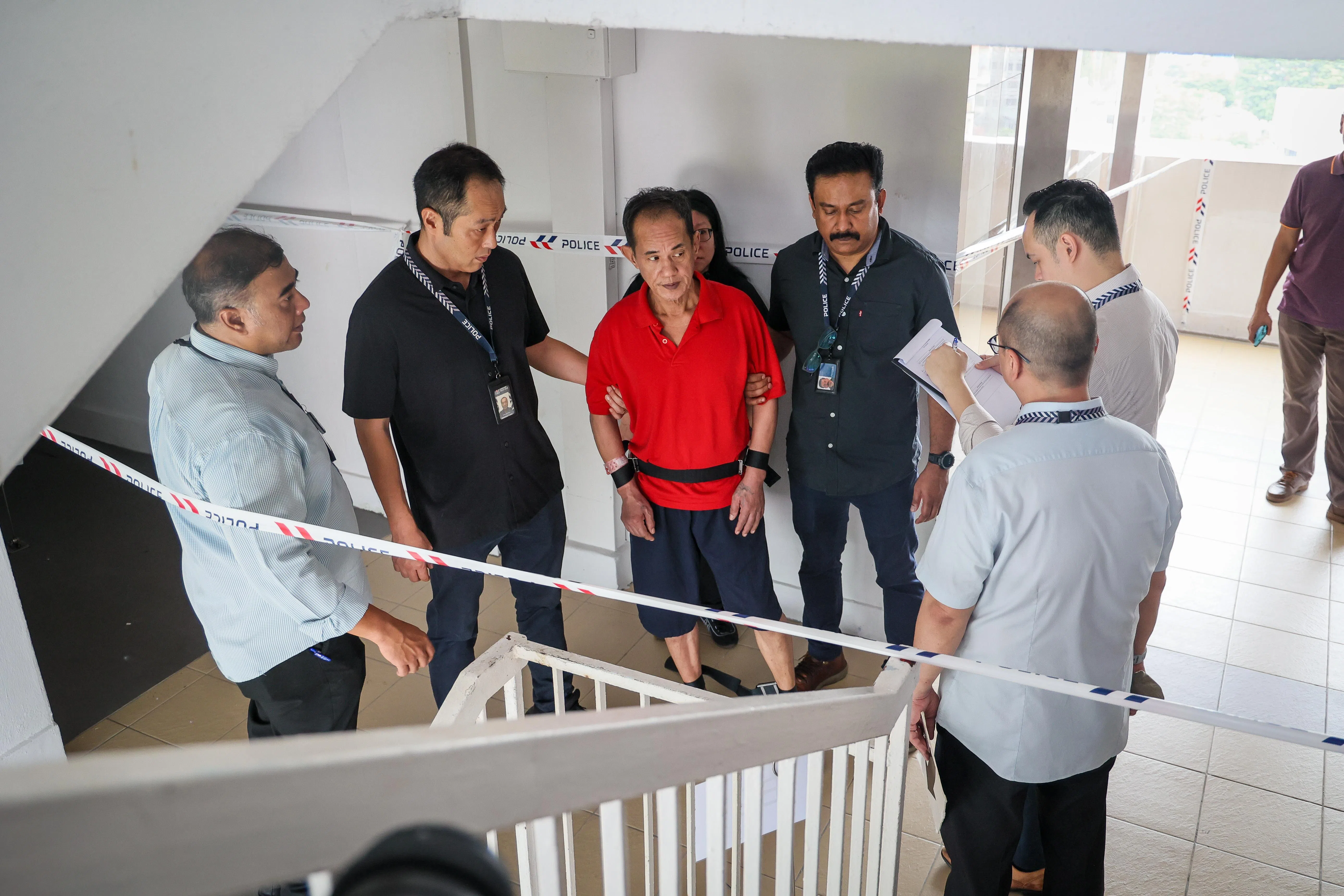 59岁的被告傅俊杰（中）被警方带到不同楼层，警方一边指着地，一边询问被告相关问题。（张俊杰摄）