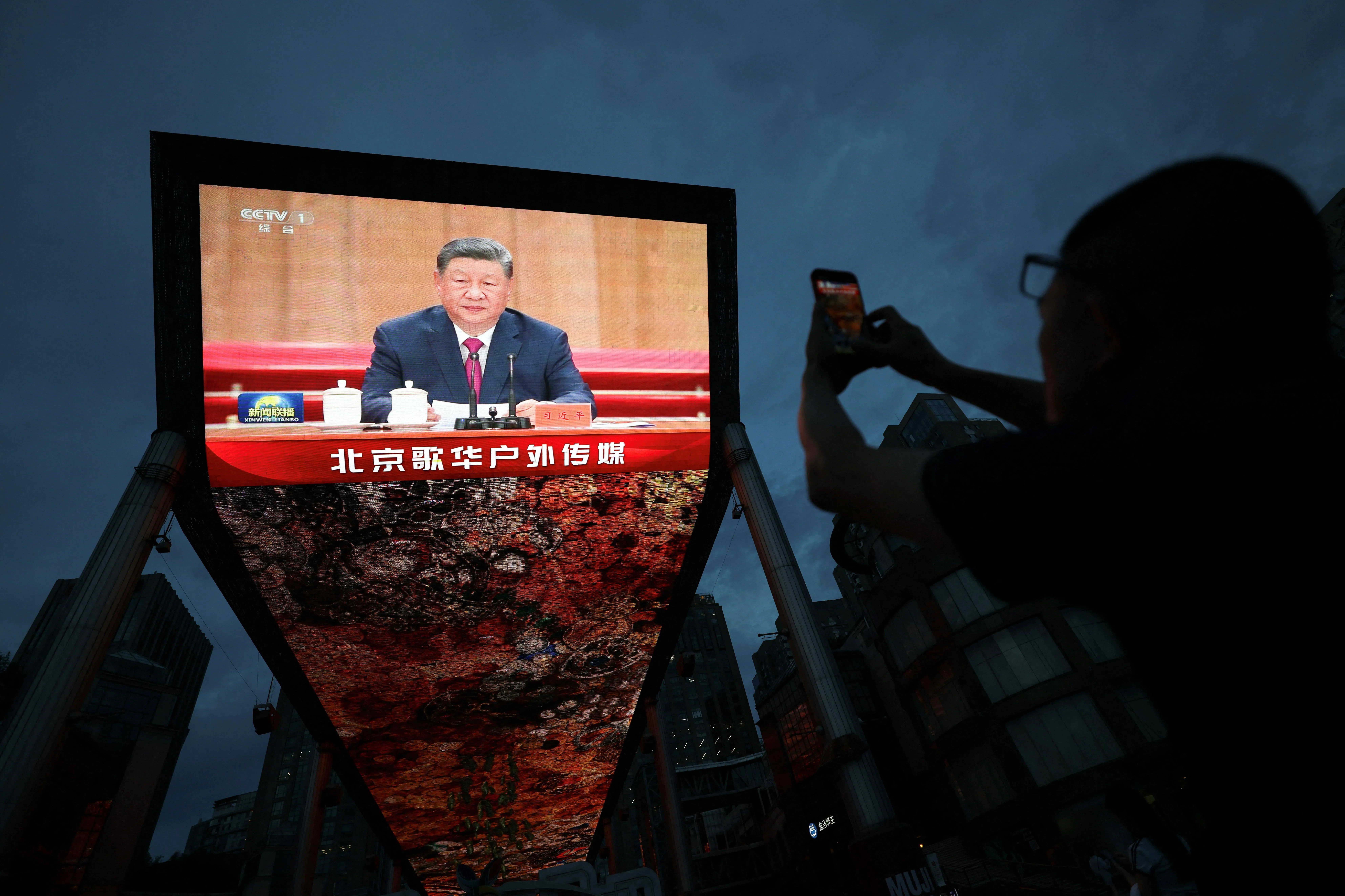 学者分析，中国官方一方面高度肯定江泽民、朱镕基时期市场化、国企改革与加入世贸等政绩，另一方面强调新时代改革须坚持中共全面领导，显示江朱改革未被否定，但国家、市场与党的角色排序已改变。图为8月17日，北京街头巨型屏幕播放中国国家主席习近平在纪念已故领导人江泽民诞辰100周年活动上的讲话，民众驻足拍摄。（路透社）
