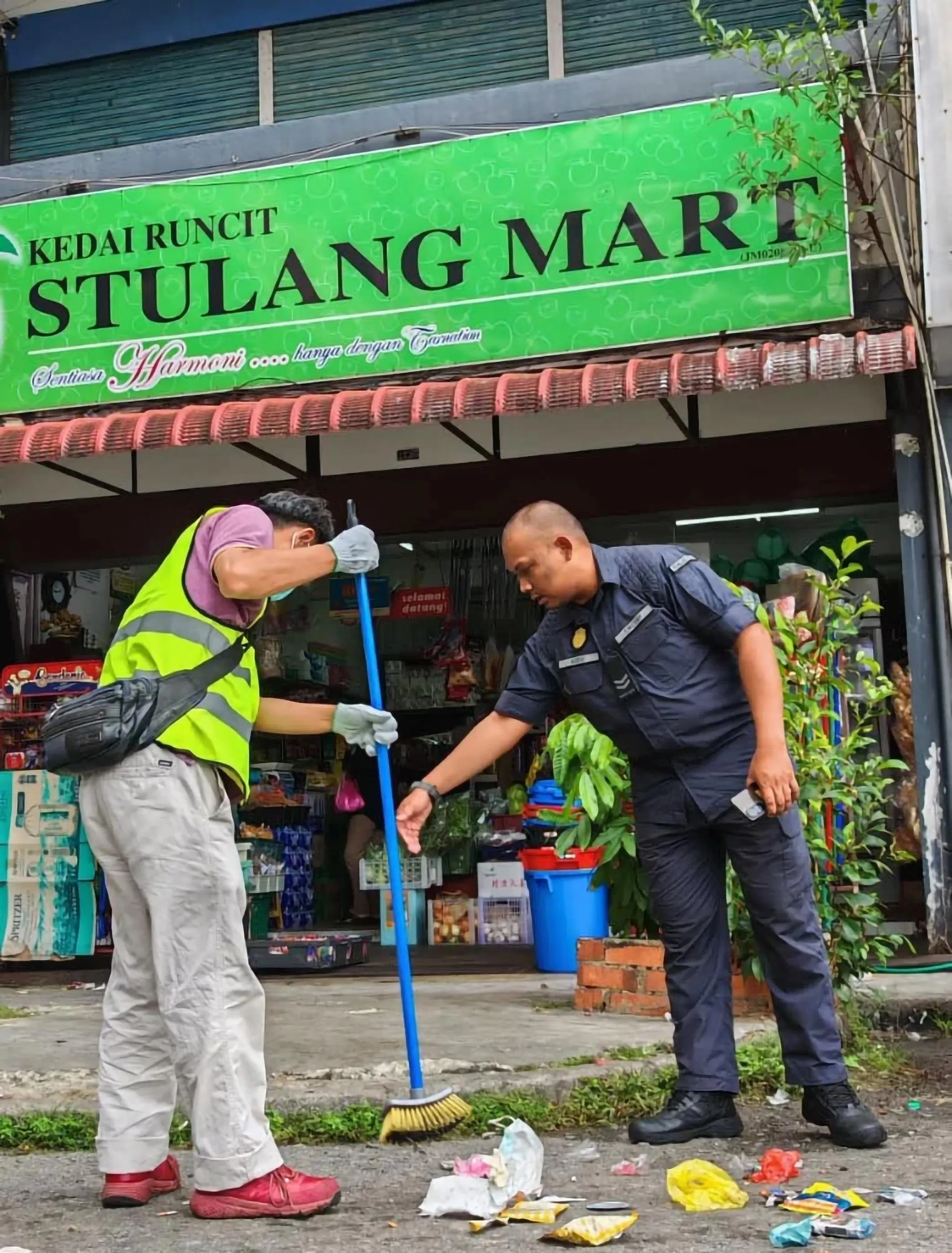 因乱丢垃圾被罚的男子（左）身穿印有“社区服务令”的反光外套，在官员监督下清扫街道。（星洲日报）