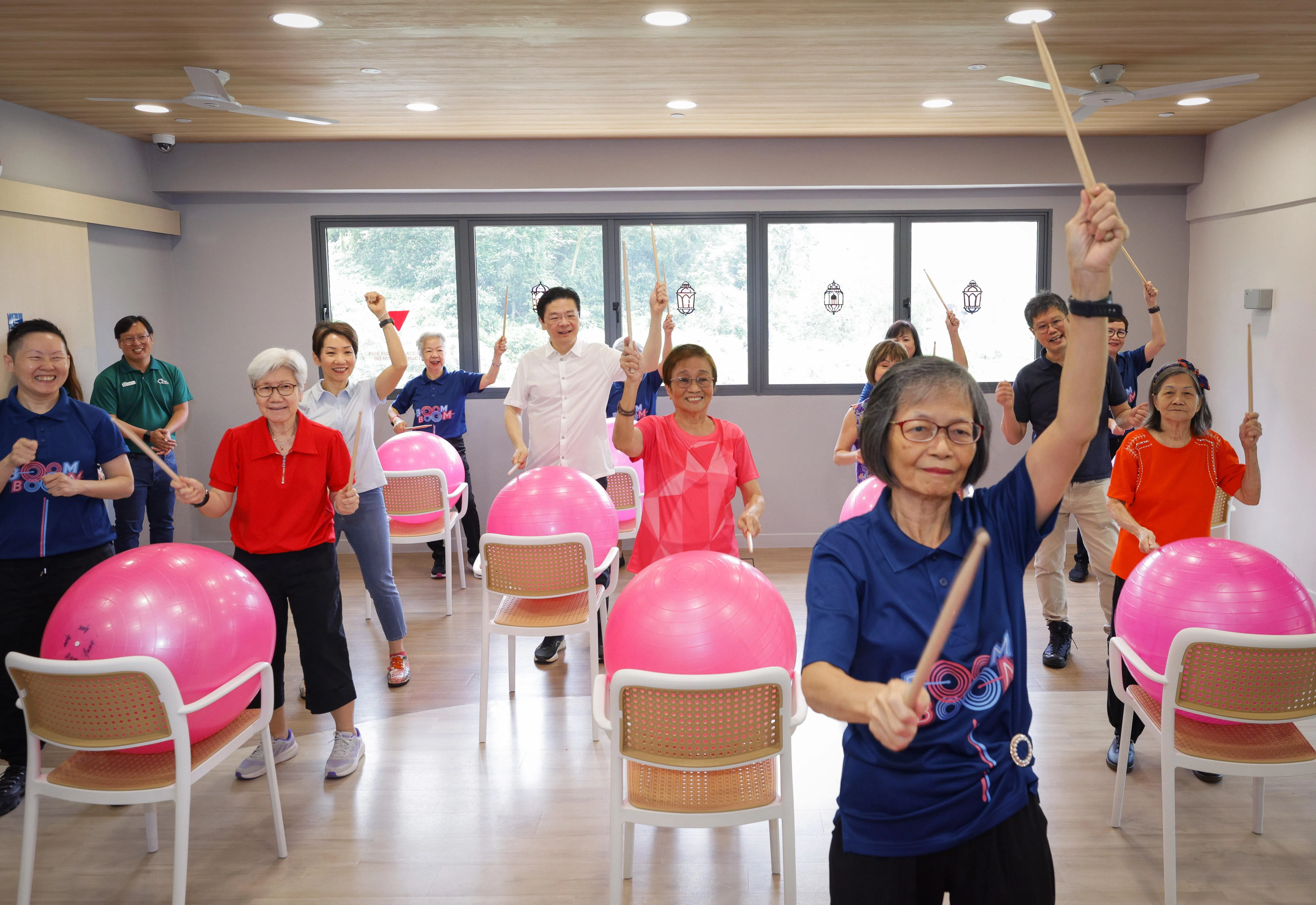 随着人口老龄化，政府致力于改善年长者的长期护理和居住安排，包括在全岛建造更多社区关爱组屋，以及设立乐龄社区。图为黄总理（左六）和永续发展与环境部长傅海燕（左四）在武吉巴督的首个社区关爱组屋项目，与年长者一起击鼓健身。（数码发展及新闻部提供）