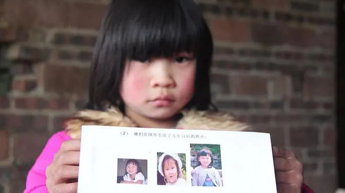 曾又东双胞胎女儿中的姐姐被抱走后，被一户美国人家收养。图为妹妹曾双洁拿着姐姐被抱走后在美国生活了几年后的照片。（财新网） 