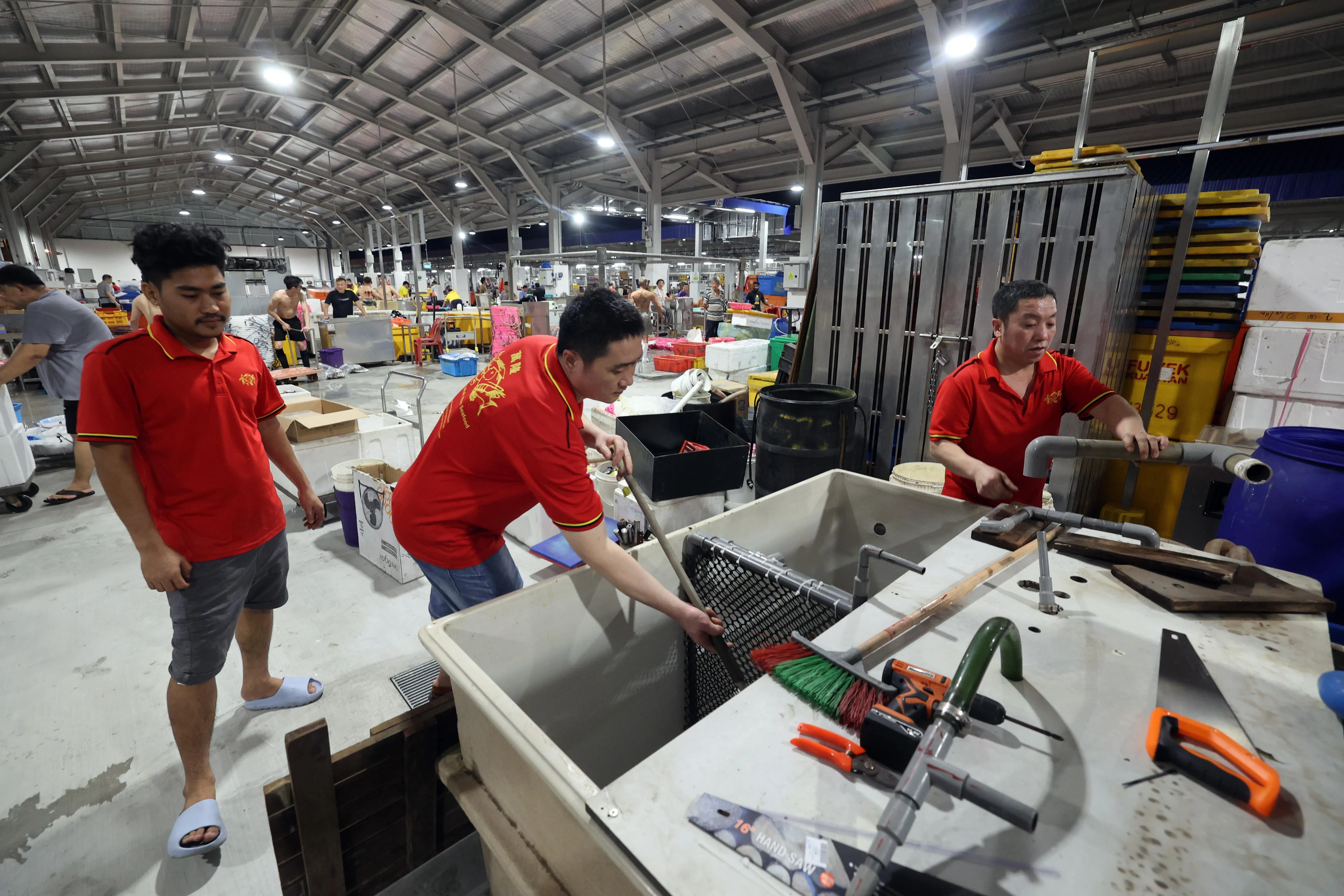 从圣诺哥渔港搬到裕廊渔港的商家万隆华和的员工，在开市第一天搭建水缸。	（邝启聪摄）