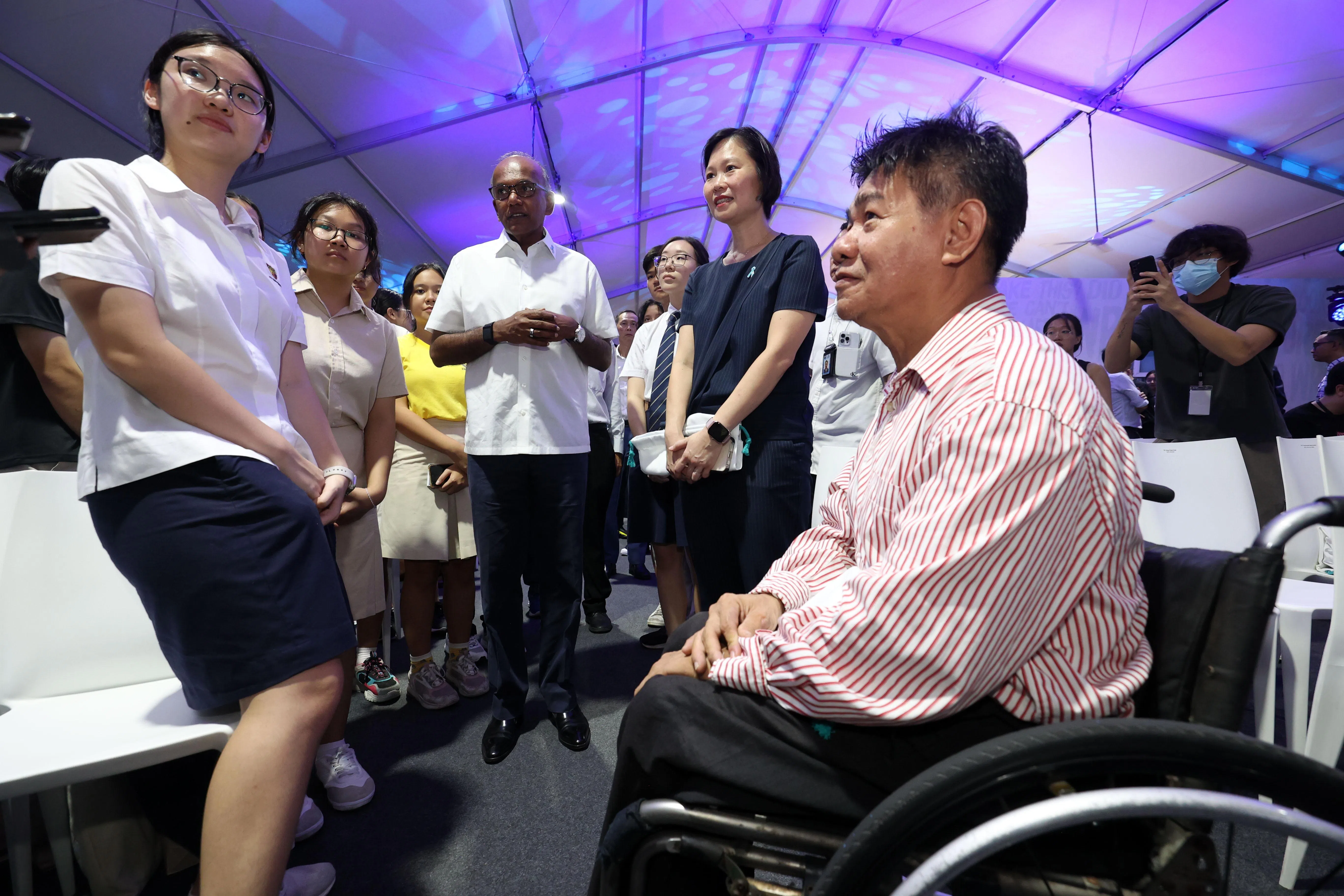 坐在轮椅上的林新新牧师向内政部长兼律政部长尚穆根（中间白衣者）、教育部兼人力部政务部长颜晓芳（中间白蓝衣者），及出席活动的学生，讲述自己沉沦毒海的往事。（邝启聪摄）