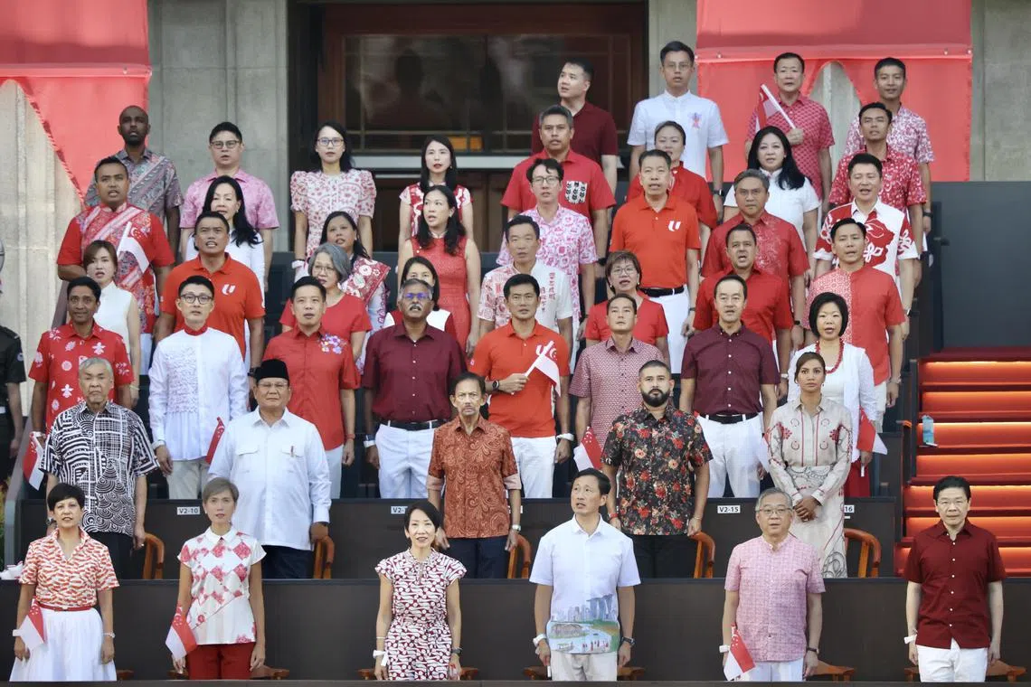 悬挂巨型国旗的直升机缓缓飞过上空，政务官和国会议员齐声唱响国歌，当中包括总理黄循财（第一排右起）、副总理兼贸工部长颜金勇、社会政策统筹部长兼卫生部长王乙康、永续发展与环境部长傅海燕、数码发展及新闻部长杨莉明，以及总理公署部长兼财政部及国家发展部第二部长英兰妮。受邀观礼的外宾有马来西亚副首相兼乡村及区域发展部长阿末扎希（第二排左起）、印度尼西亚总统普拉博沃、文莱苏丹波基亚，以及马国柔佛王储东姑依斯迈和王储妃卡丽达。（邝启聪摄）