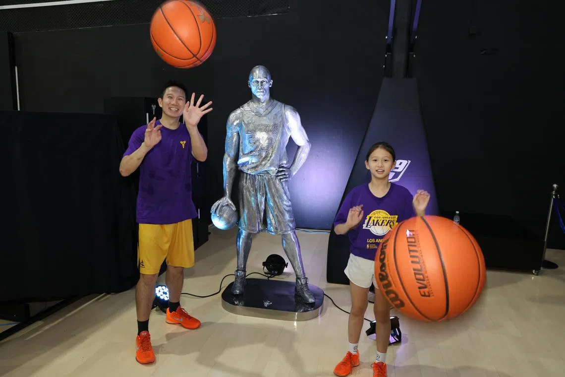 40岁的黎威杰（左）和11岁女儿黎瑞恩与雕塑合影，两人一同搭档参加了亲子投篮比赛。（梁麒麟摄）