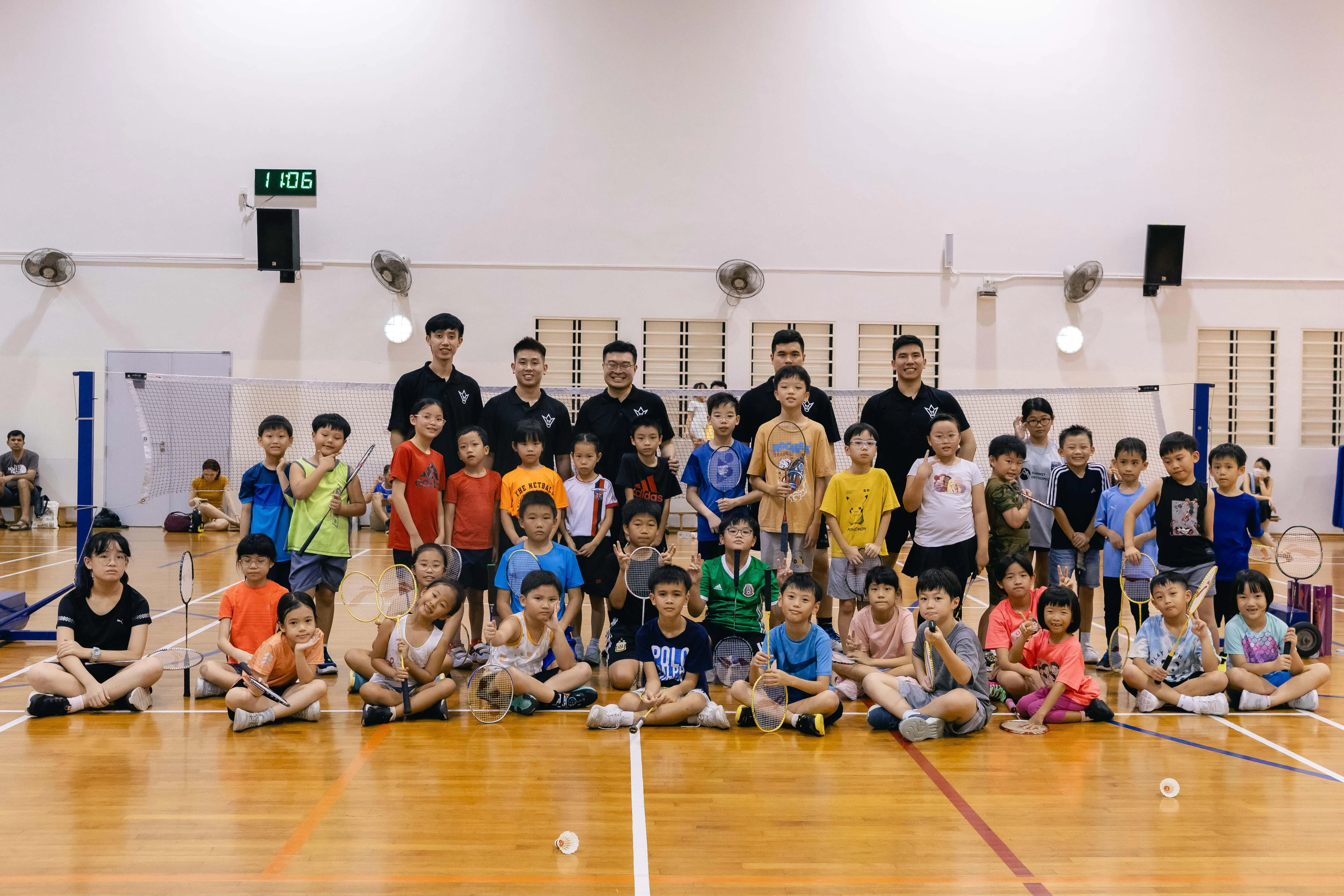 骆建贤（后排左二）与好友黄靖安（后排左一）合办羽毛球学院，向没有将羽毛球作为课外活动的小学推广这项运动。（黄靖安提供）