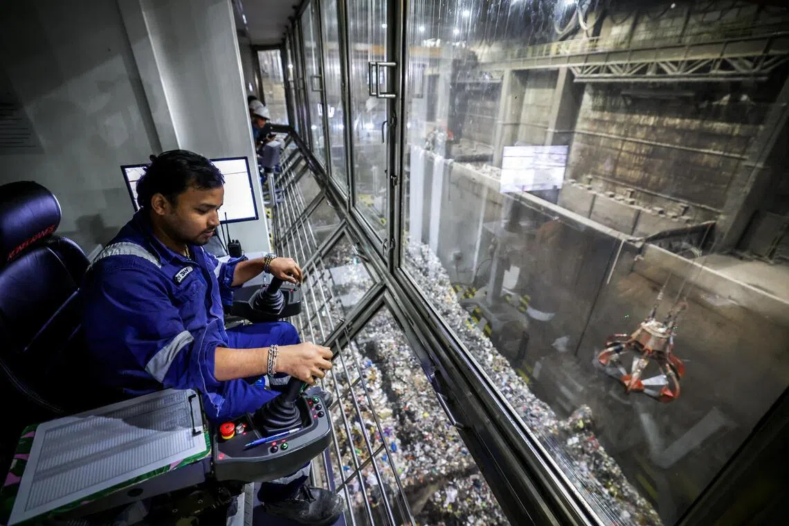 在TuasOne废料转化能源厂，工作人员正在用操纵杆操作巨爪机器混合垃圾，也把大型垃圾分离开来。TuasOne每天可焚化3600公吨的垃圾，生产约120兆瓦的电力，足以为24万个四房式组屋单位供电。（叶振忠摄）