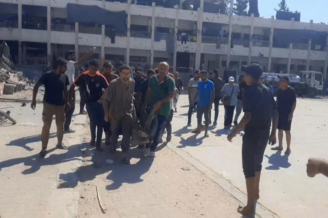 幸存的巴勒斯坦人将伤患抬离遇袭校园。（路透社）