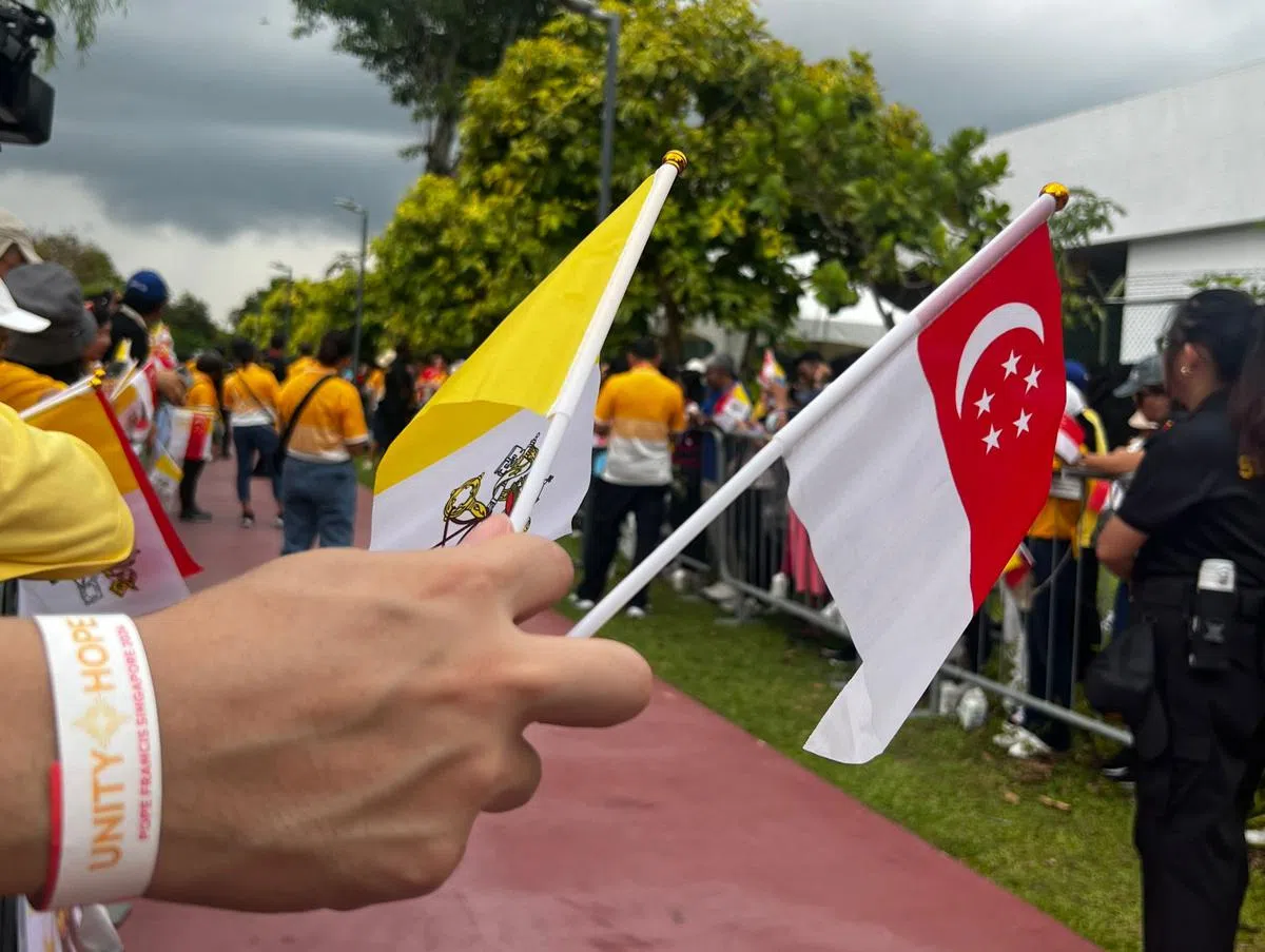 不少信众穿着黄色的纪念衫，手持新加坡与梵蒂冈的小旗，等候间隙与身旁人交谈、合影。（杨烨摄）