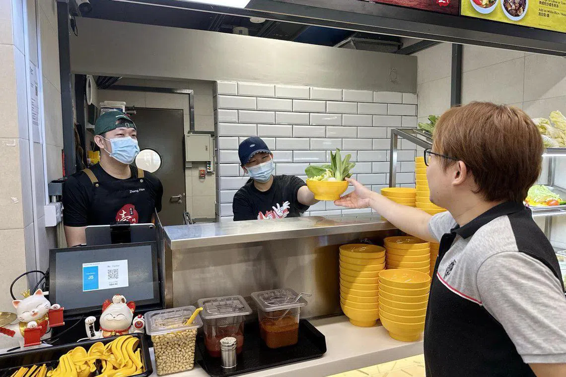 没上课或学习的时候，王政翰（左一）就会到大学食阁摊位工作。女友黄炯雯有空时也会前去帮忙。（新加坡理工大学提供）