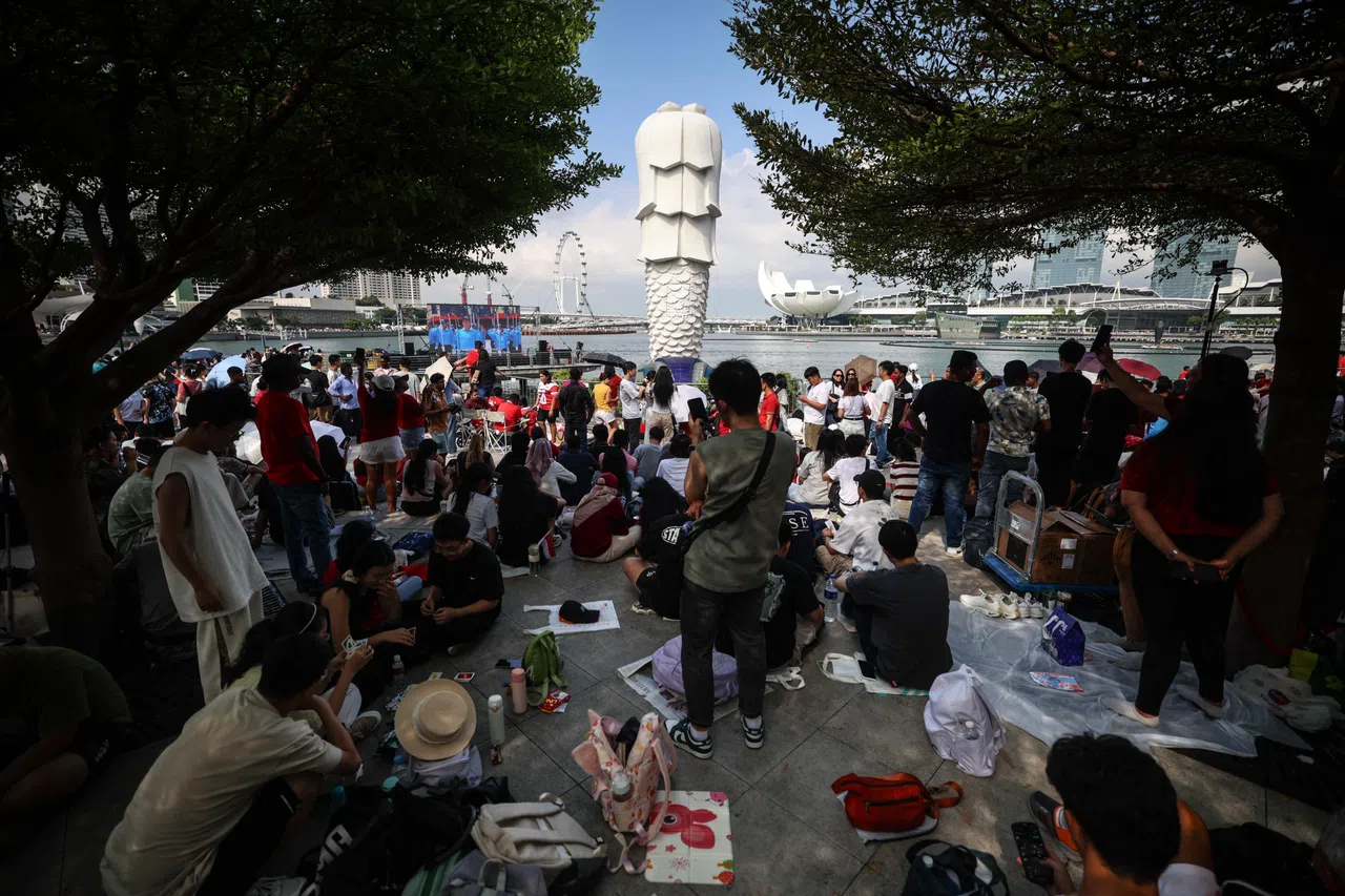 今年国庆庆典的舞台延伸至滨海湾，不少公众早早来到鱼尾狮公园占据好视角，与亲朋好友相聚野餐，欢声笑语间等待演出开场。（关俊威摄）