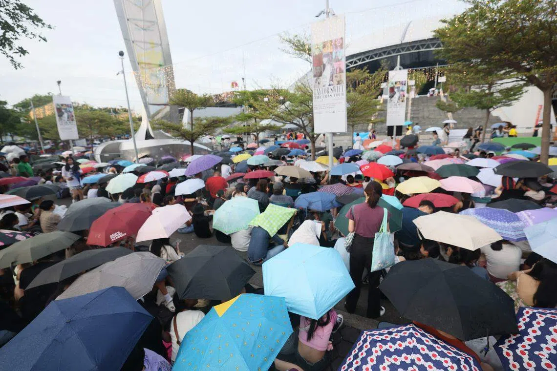 下午3时前往体育馆时正下着大雨，场外却已有大批粉丝聚集，一边排队购买泰勒丝的周边商品，一边跟随音乐大合唱，场面欢腾热烈。（郑一鸣摄）