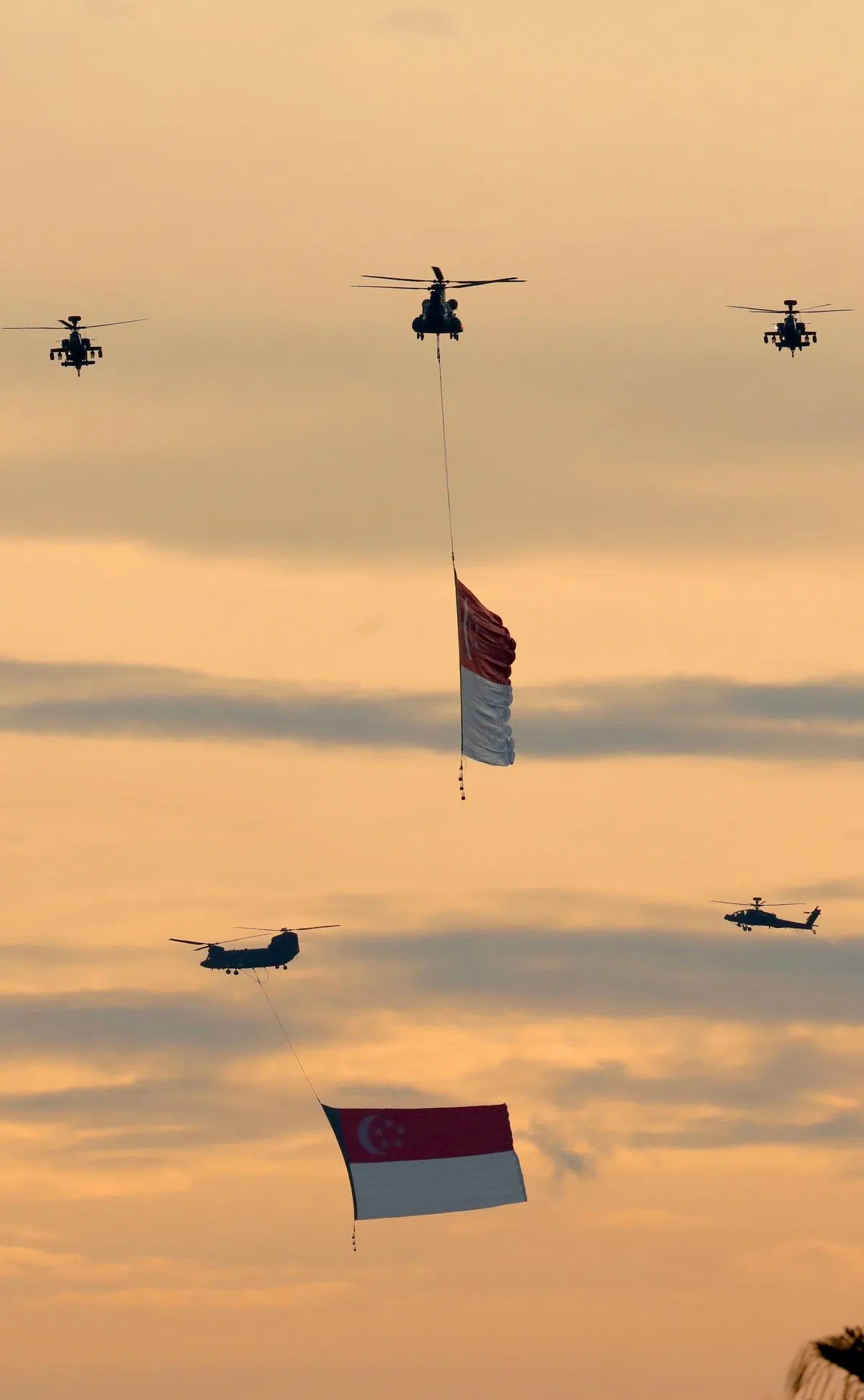 两架悬挂巨型国旗的契努克（Chinook）直升机，飞越滨海湾上空。（何家俊摄）