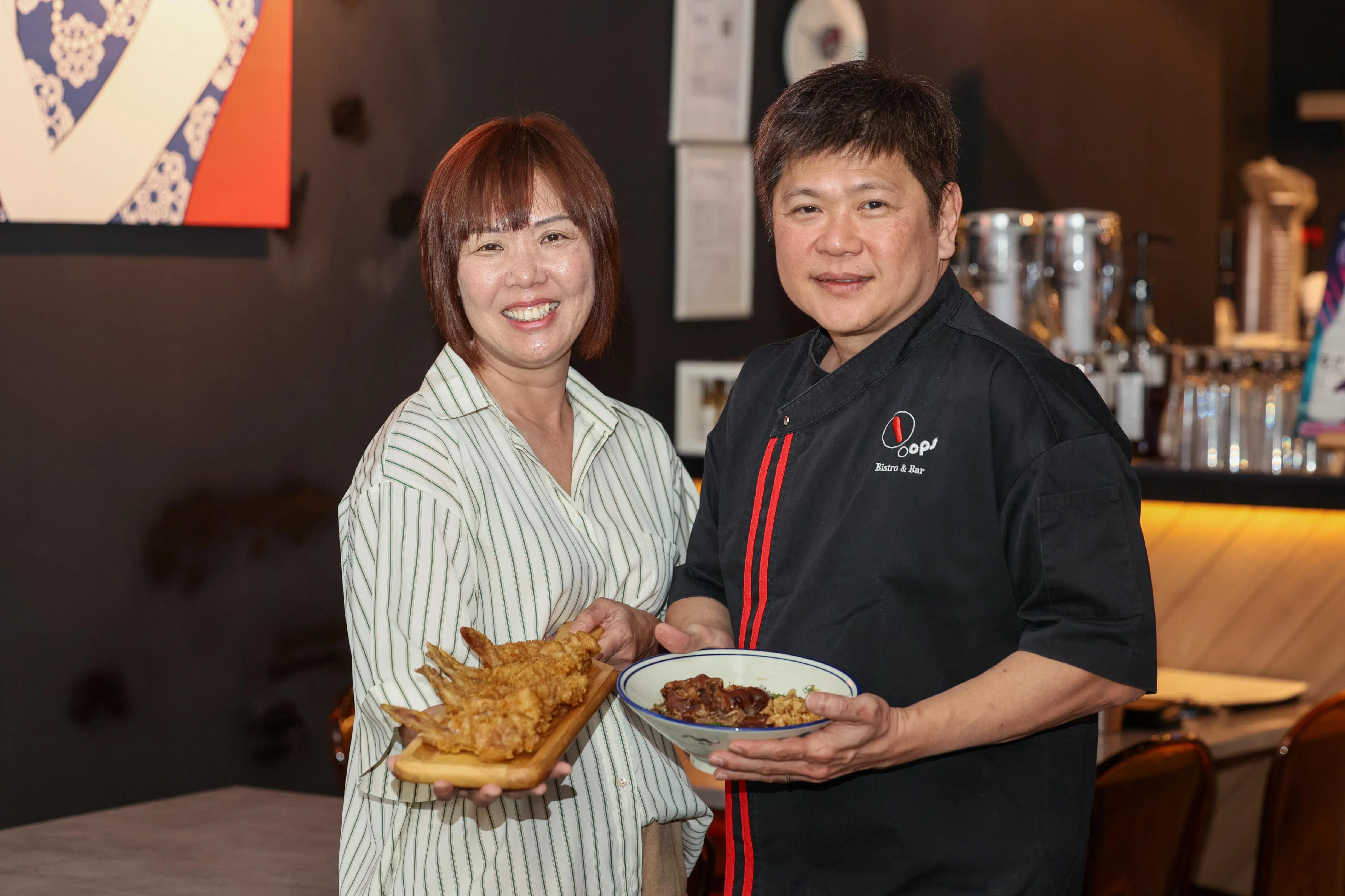 黄竟财（右）推出猪脚米粉和去骨虾酱鸡翅等多道本地佳肴，妻子方娟娟（左）则负责招待客人和制作甜品。（卓祾祎摄）