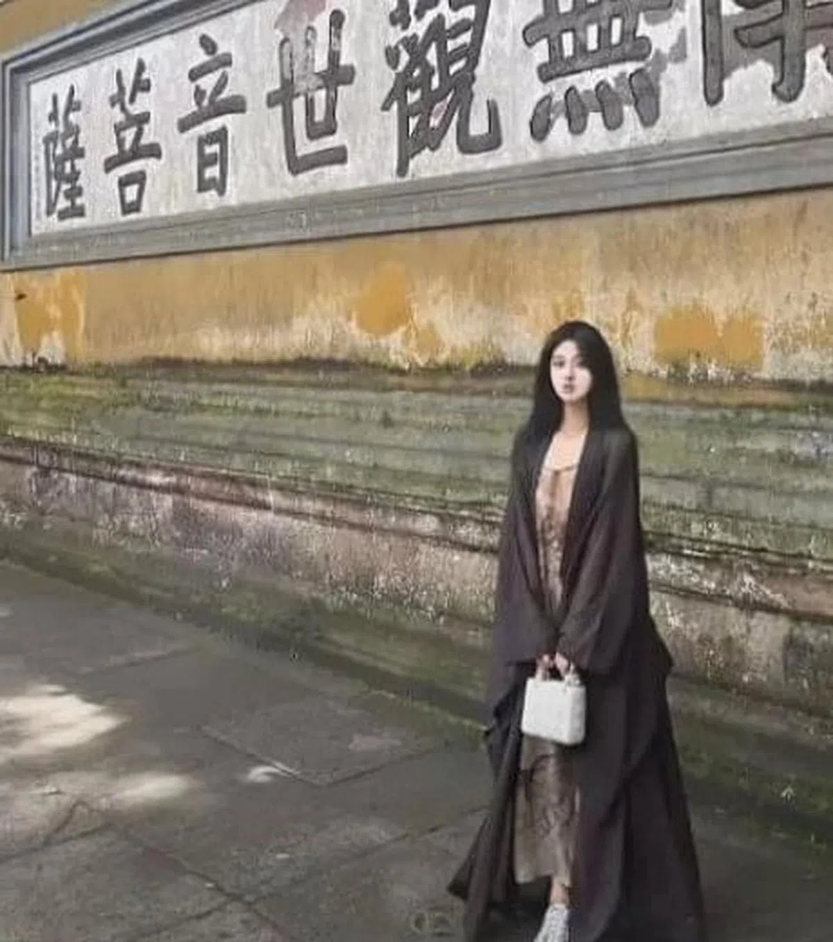 一名佛媛将海青（礼佛时穿的衣服）当作配饰随意披挂身上，站在舟山普济市门口的“南无观世音菩萨”字样前拍照，手上还提着一只白色Dior包。（互联网）