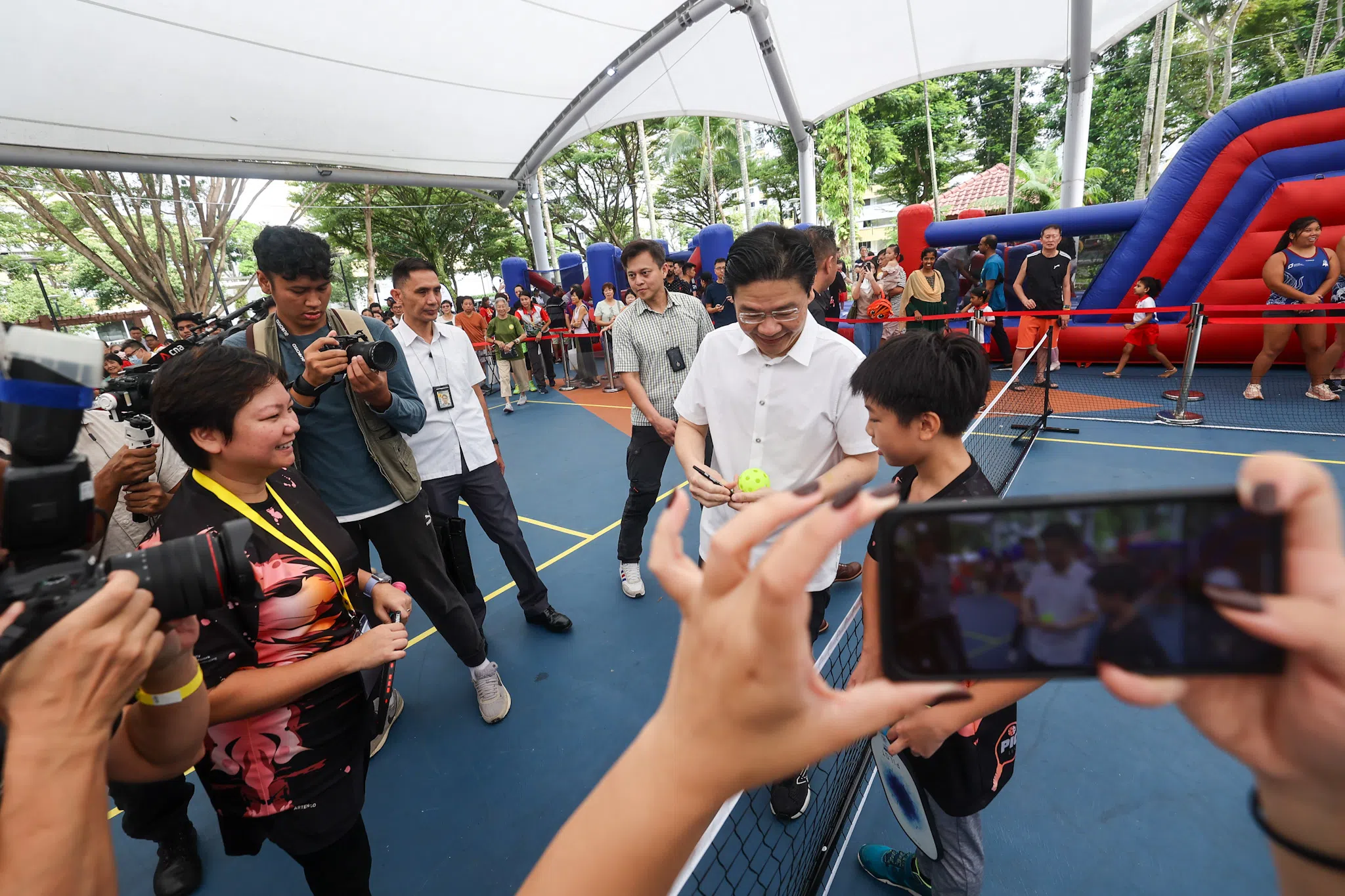 黄总理（右二）在活动上学习如何打匹克球，并为洪睿沣（右一）在一个匹克球上签名。洪睿沣每周都会与母亲、匹克球兴趣小组负责人陈欣慧（左一）一起打匹克球，如今他还会充当老师教其他年长者如何打球。（陈渊庄摄）