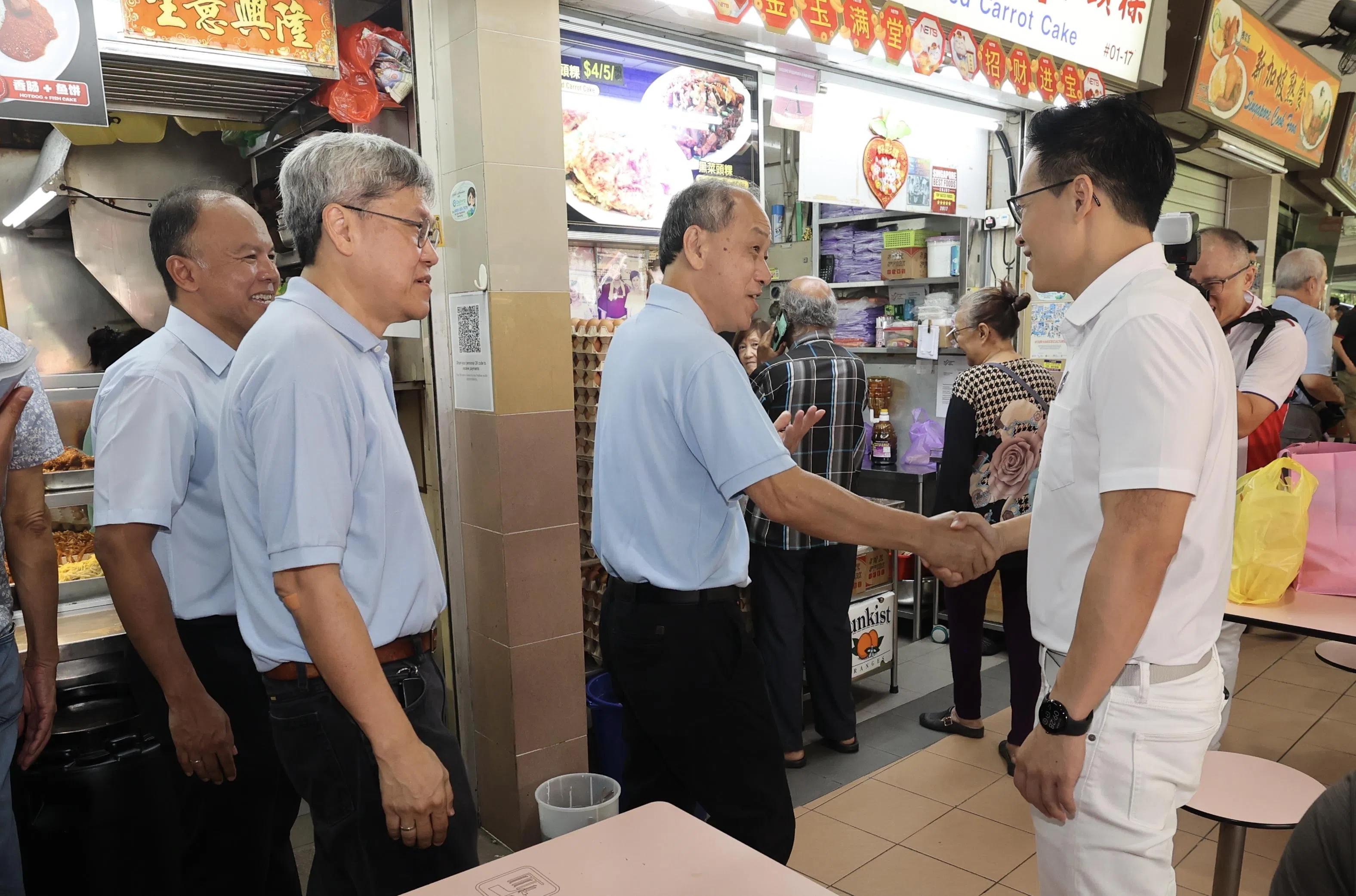 工人党前秘书长刘程强（右二）和前议员方荣发（左二），星期六连同费沙（左一）领导的工人党淡滨尼团队一起走访淡滨尼圆巴刹与熟食中心时，碰上行动党淡滨尼尚育区候选人朱倍庆（右一），并与他握手问候。（邬福梁摄）