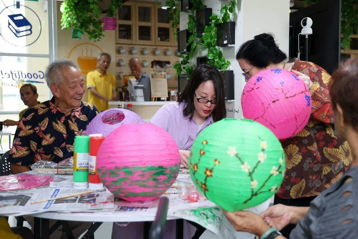 黄国松（左）和未婚妻刘以真（中）在马林台第52座组屋底层的“快乐中心”（Goodlife! Makan）社区厨房，同乐龄人士一起制作灯笼。（林明顺摄）