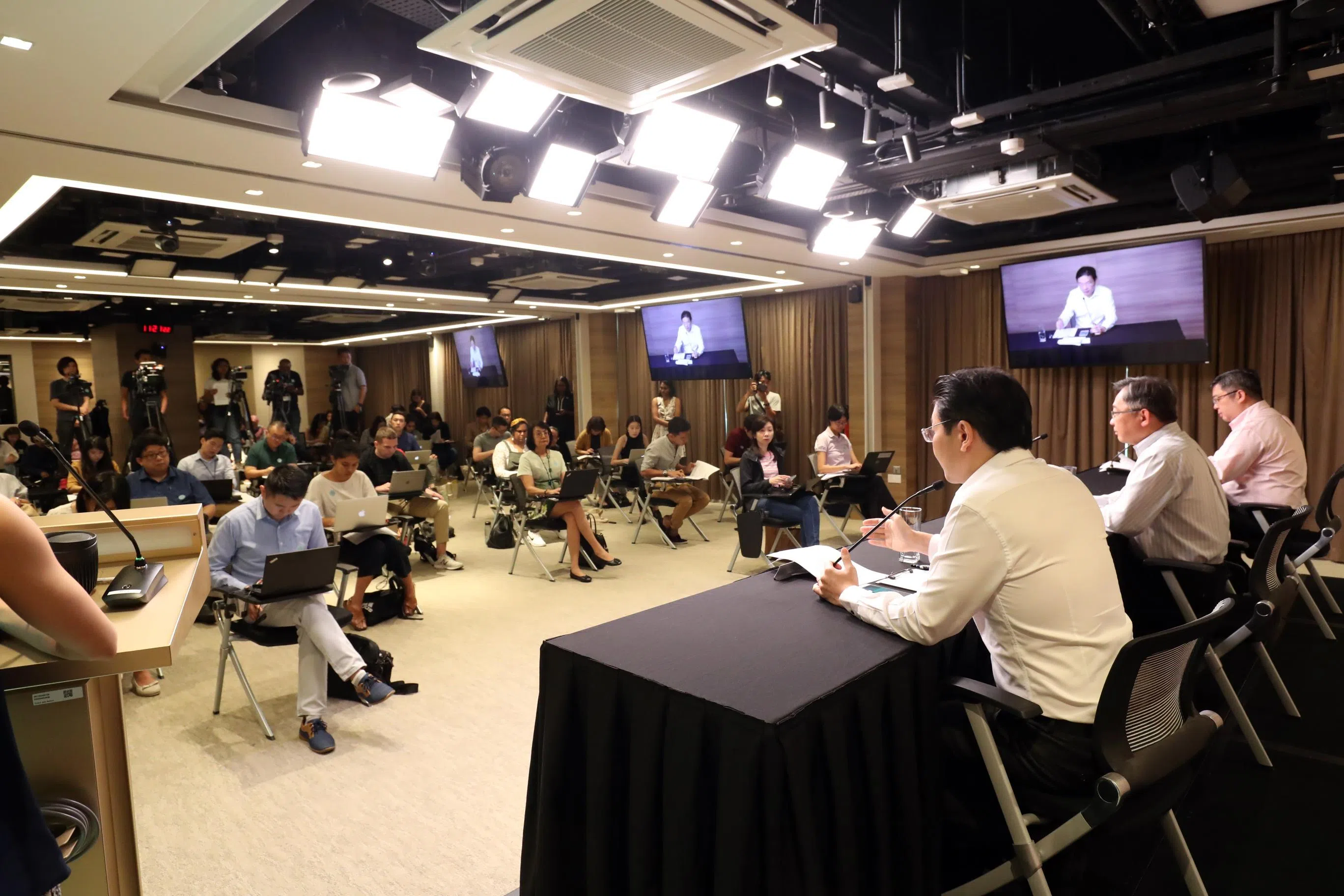 为减少社交接触，抗疫跨部门工作小组记者会于2020年3月13日首次安排记者拉开距离来坐，代表早报采访组的医药线组长刘智澎（前左一）参加了这场记者会。国家发展部长兼财政部第二部长黄循财（背向镜头左一）、卫生部长颜金勇（中）及卫生部医药服务总监麦锡威副教授（右一）之间也保持约一米的安全距离。（档案照片）