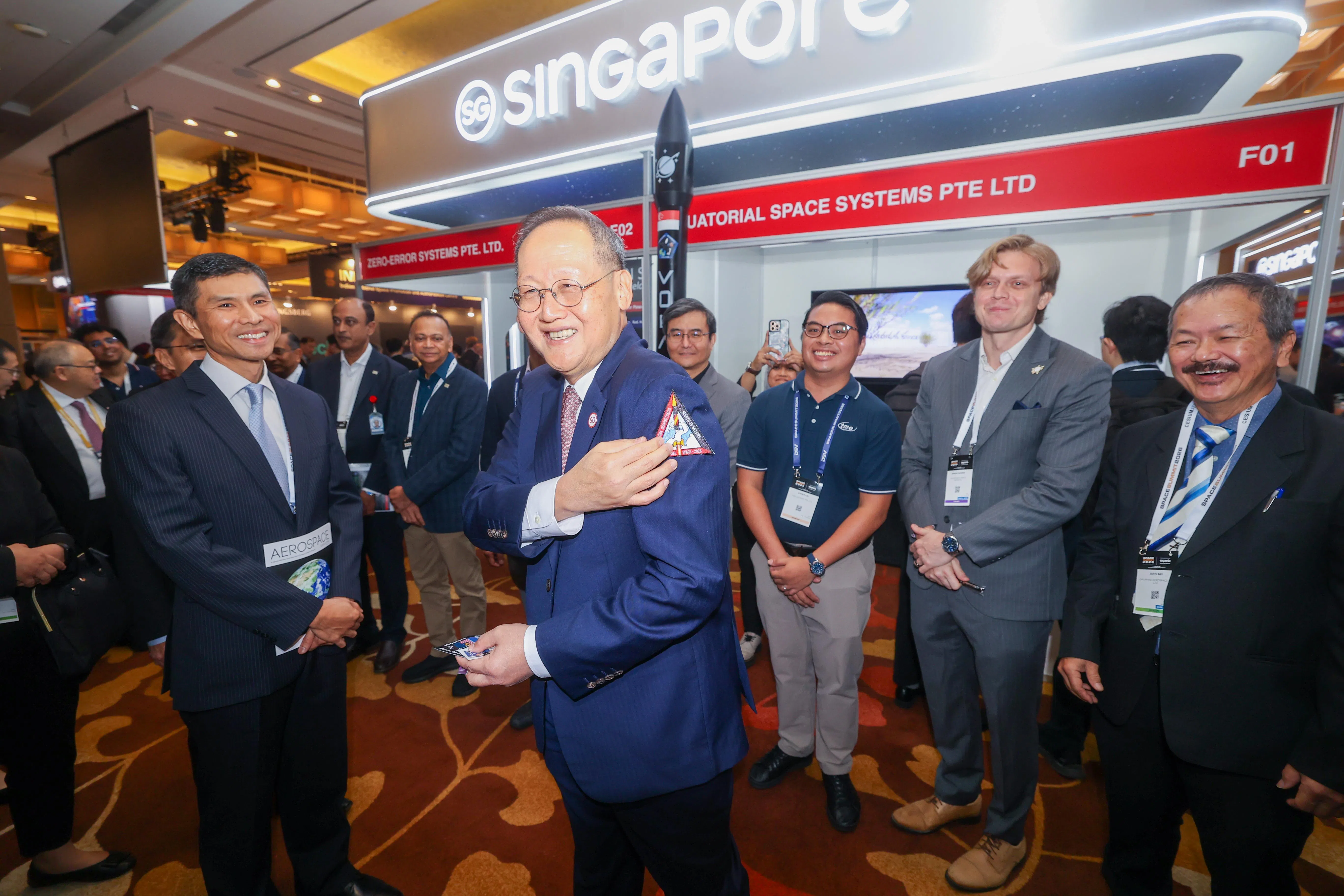 主管能源与科技事务的人力部长陈诗龙医生（左二），星期一为首届航天峰会主持开幕后，走访现场企业摊位，并试戴航天公司Equatorial Space的徽章。左一为新加坡航空航天工业协会首席执行官周辉扬。（吴先邦摄）