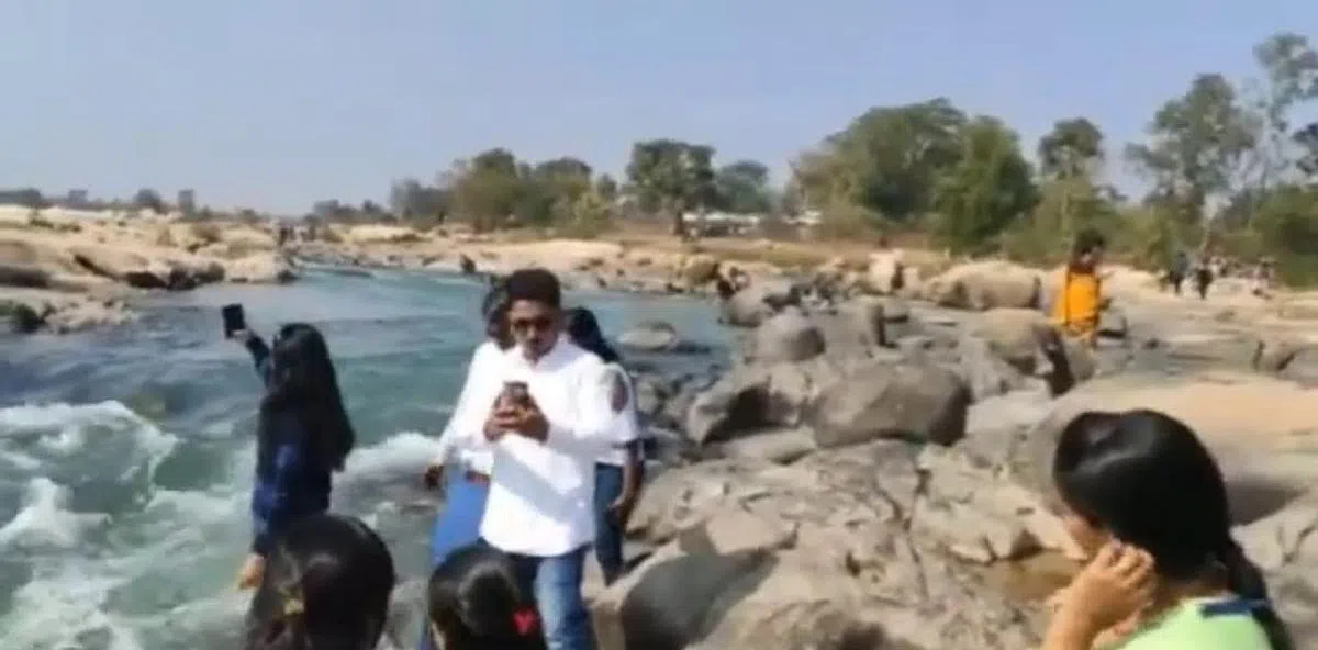 岸边挤满了人，事发前黑衣女子站在河沿上（也可能是河里）举起手机自拍。（视频截图）