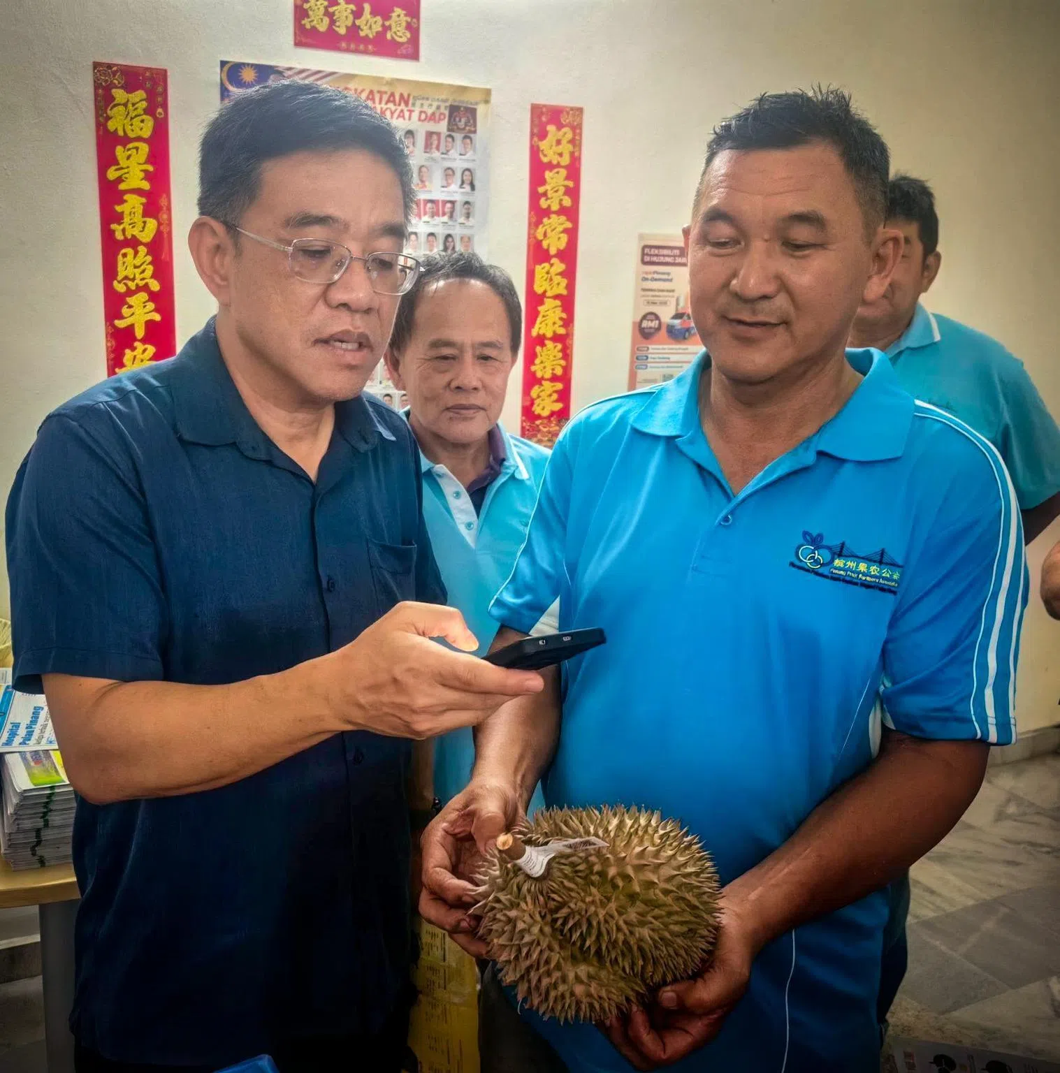 槟州旅游及创意经济事务行政议员黄汉伟（左）示范如何扫描附在榴梿上的二维码，查看榴梿产地等信息。（取自黄汉伟脸书）