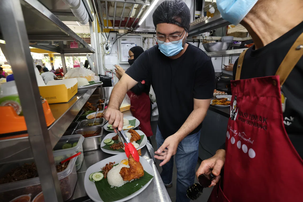 义顺居民诺曼（中）从义顺公园小贩中心起家，如今他和妻子打造的马来椰浆饭品牌拥有28个摊位，遍布全岛，包括著名景点滨海湾花园的食阁。（梁麒麟摄）