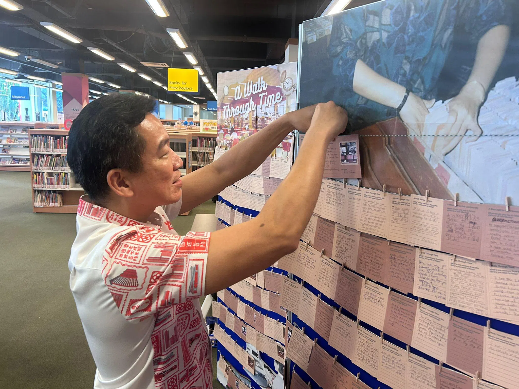 女皇镇区议员蔡瑞隆写下对女皇镇图书馆的感言，亲自把感言卡系在入馆处的感言板上。（张俊摄）
