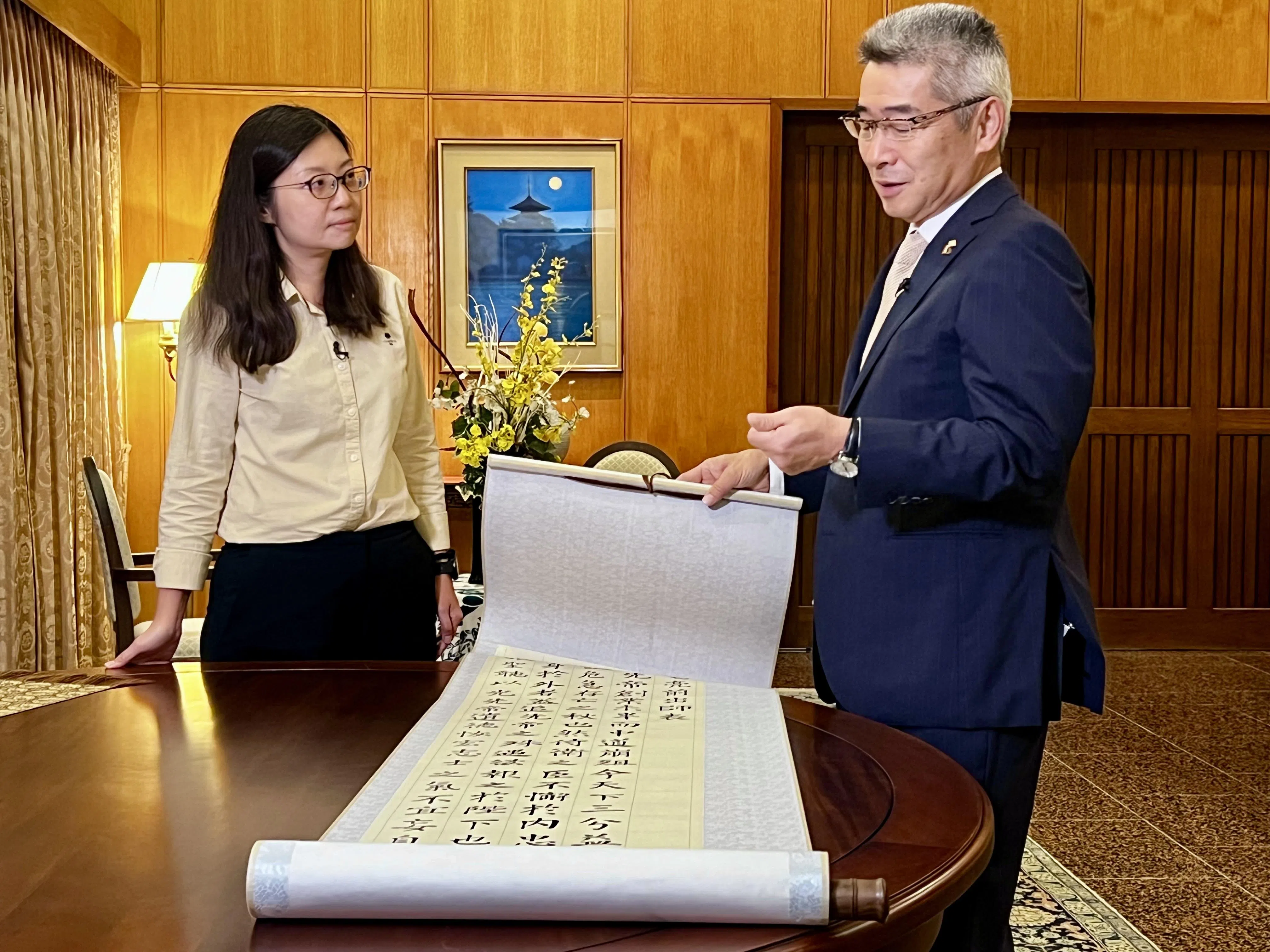 日本大使石川浩司（右）向《联合早报》视频编导许淑美展示他的书法作品，内容取自诸葛亮《出师表》首段，他表示内容“很令人感动”。（吴汉钧摄）