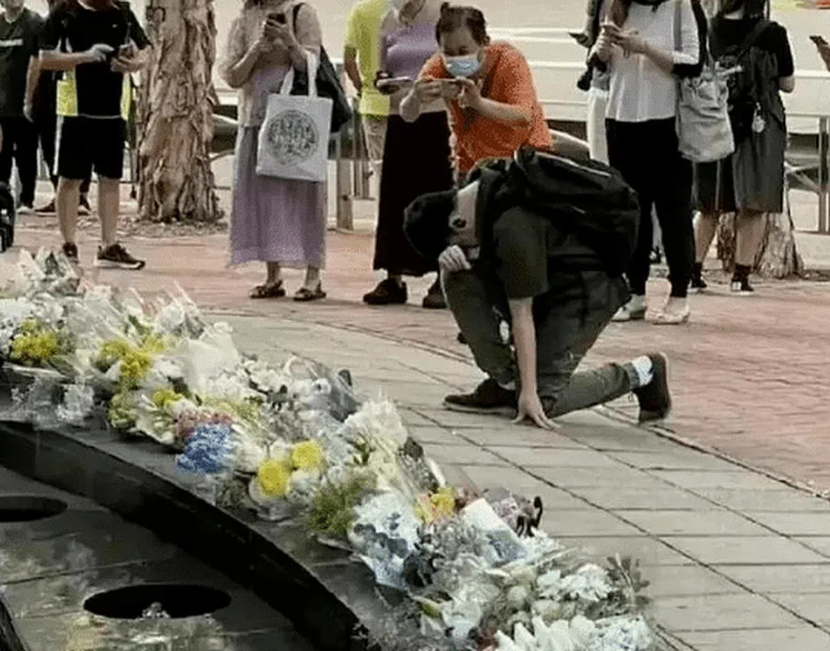 网传图片中，一名黑衣青年在民众哀悼英女王的花束前单膝跪地，低头默哀，引发大量网民对“恋殖”心态的嘲讽。（互联网）