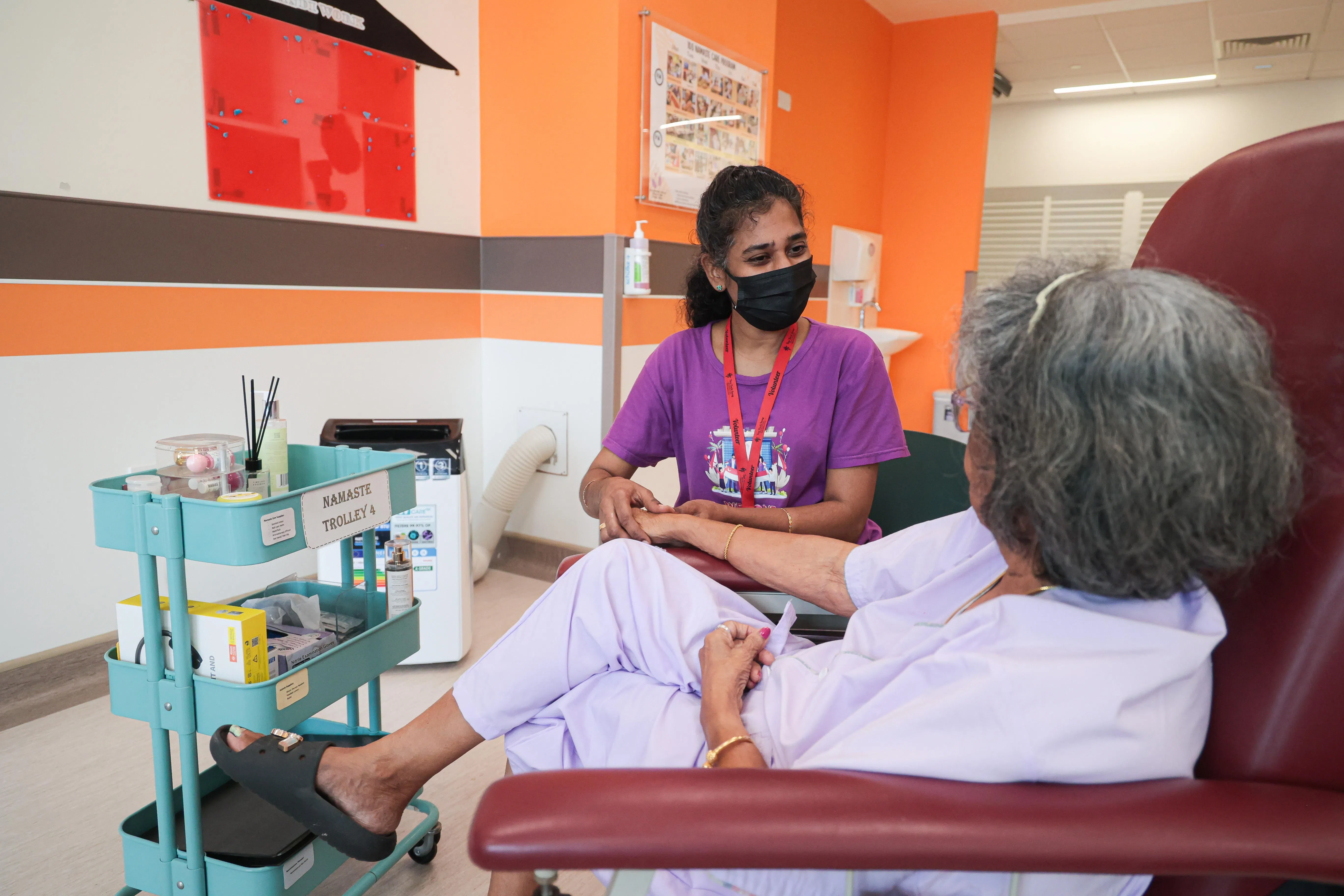 在陈笃生医院，维吉一边和失智症病患聊天，一边为她按摩手臂。（李冠卫摄）