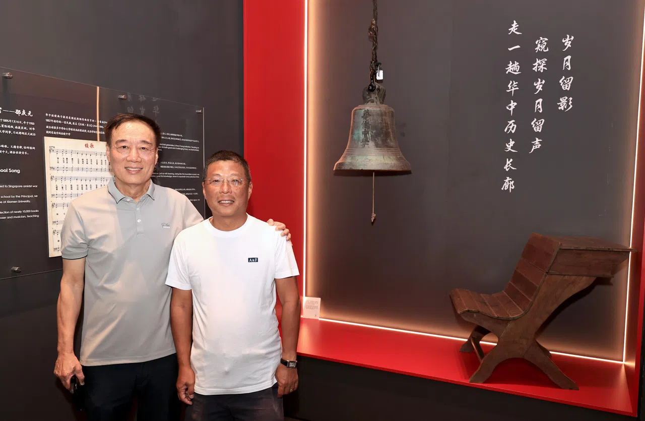 华中文物馆入口处首次展示一个使用70多年的旧校钟，以及一张早年课室使用的木桌。图为华中特别项目处长陈鹏仲（左）和校友会秘书长黄仕文在文物前合影。（周国威摄）