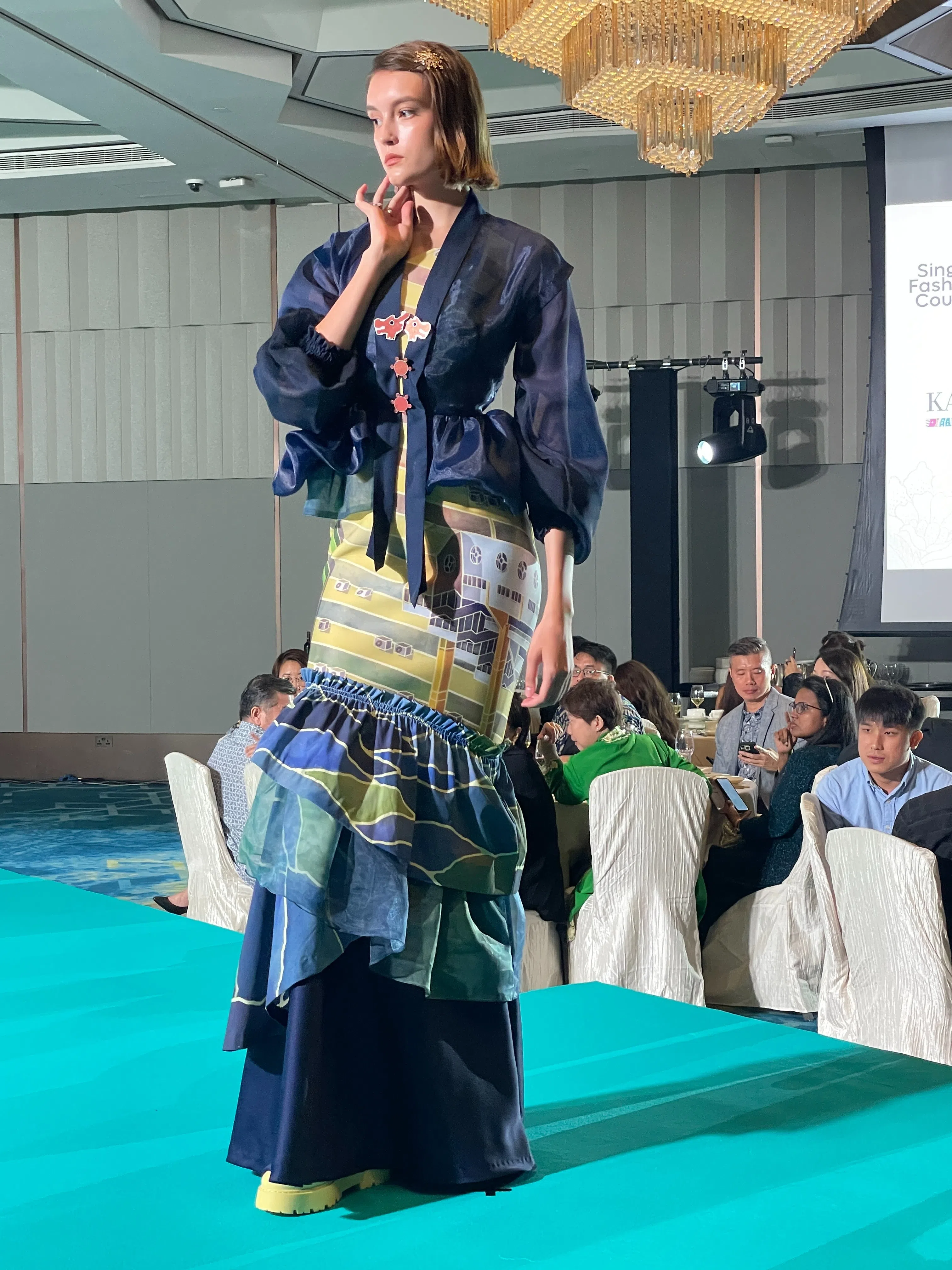 林羽嫣将组屋的图像手绘在美人鱼尾连身裙上，透过半透明的卡峇雅，若隐若现。扣住卡峇雅的胸针是旧游乐场的龙头造型。（林方伟摄）