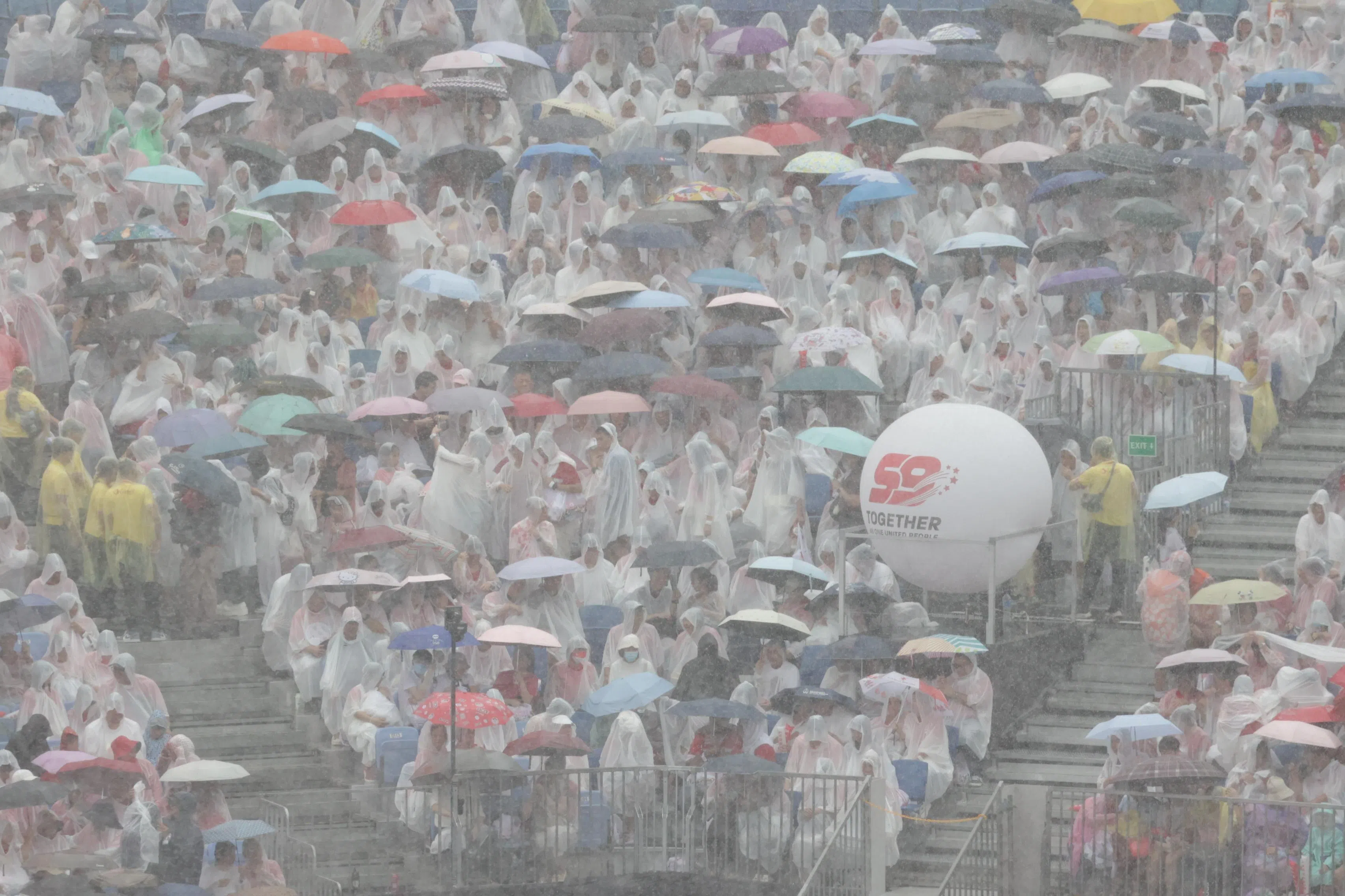 距离国庆庆典开场不到一小时，现场突降暴雨，但民众热情不减，依旧在位子上等候。（陈渊庄摄）