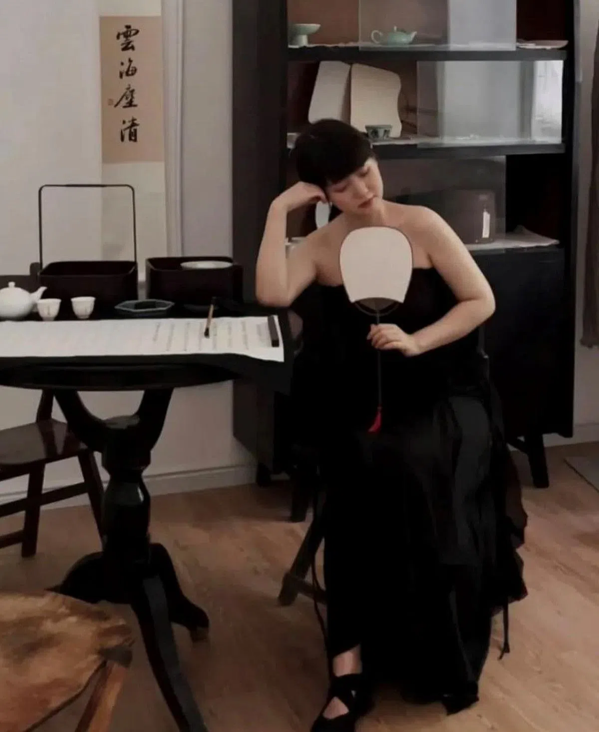 一名佛媛手持团扇，身着抹胸装，在写着经文的书桌上佯装伏案沉思。（互联网）