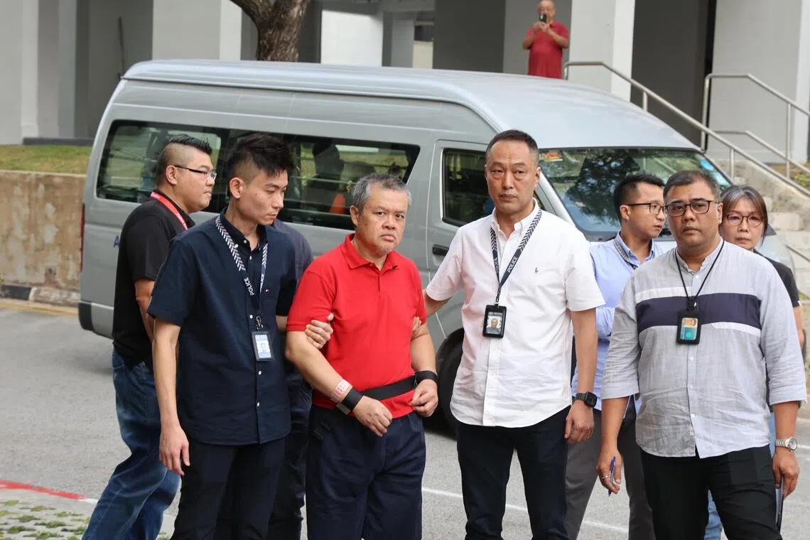 身穿红色上衣和蓝色短裤的被告黄瑞成，在约六名警员押送下抵达现场。（邝启聪摄）