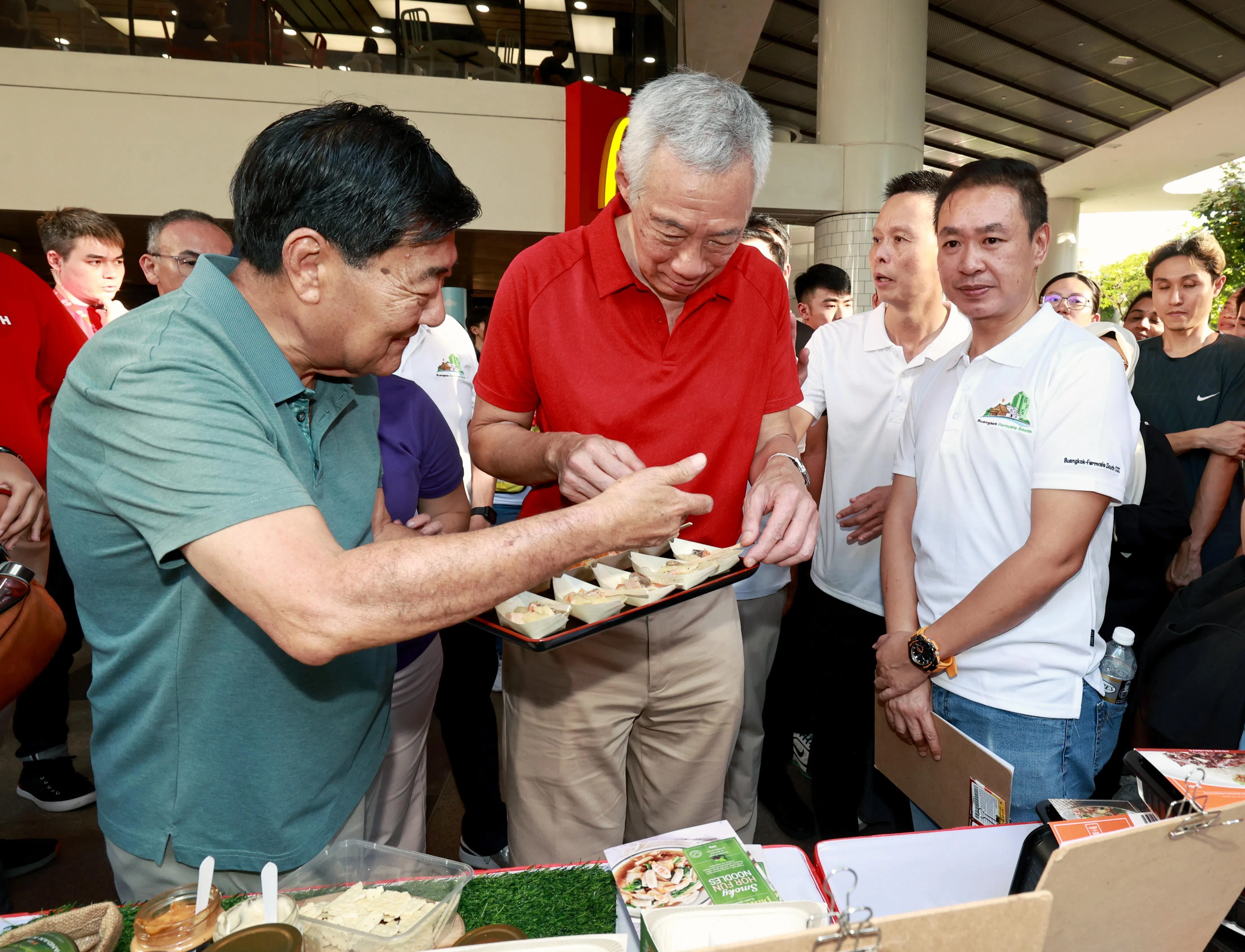 本地餐饮服务公司CHEF-IN-BOX总经理唐武光（左），为李显龙资政（中）介绍设在组屋公共区域的自动餐食贩卖机提供的餐食。（周国威摄）