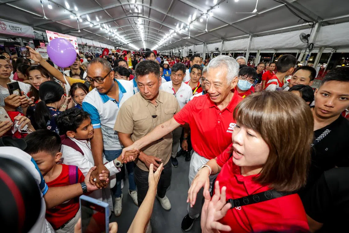 国务资政李显龙（第一排右二）星期六抵达碧山的国庆邻里嘉年华现场时，公众欣喜不已，纷纷围上去希望与他拍照握手。李资政也笑容满面，尽可能答允公众拍照留念的要求。（叶振忠摄）