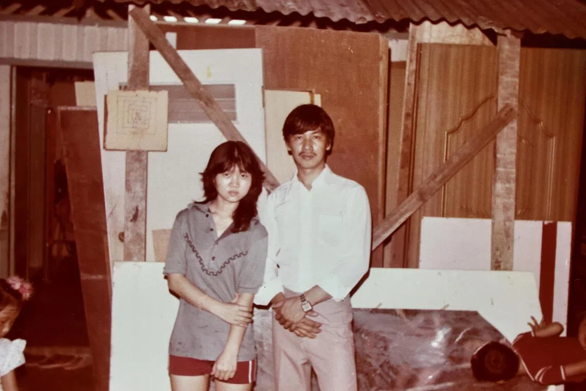 梁美石（右）和妹妹梁美招在甘榜锌板住家外的简陋“家具厂”合影。（受访者提供）