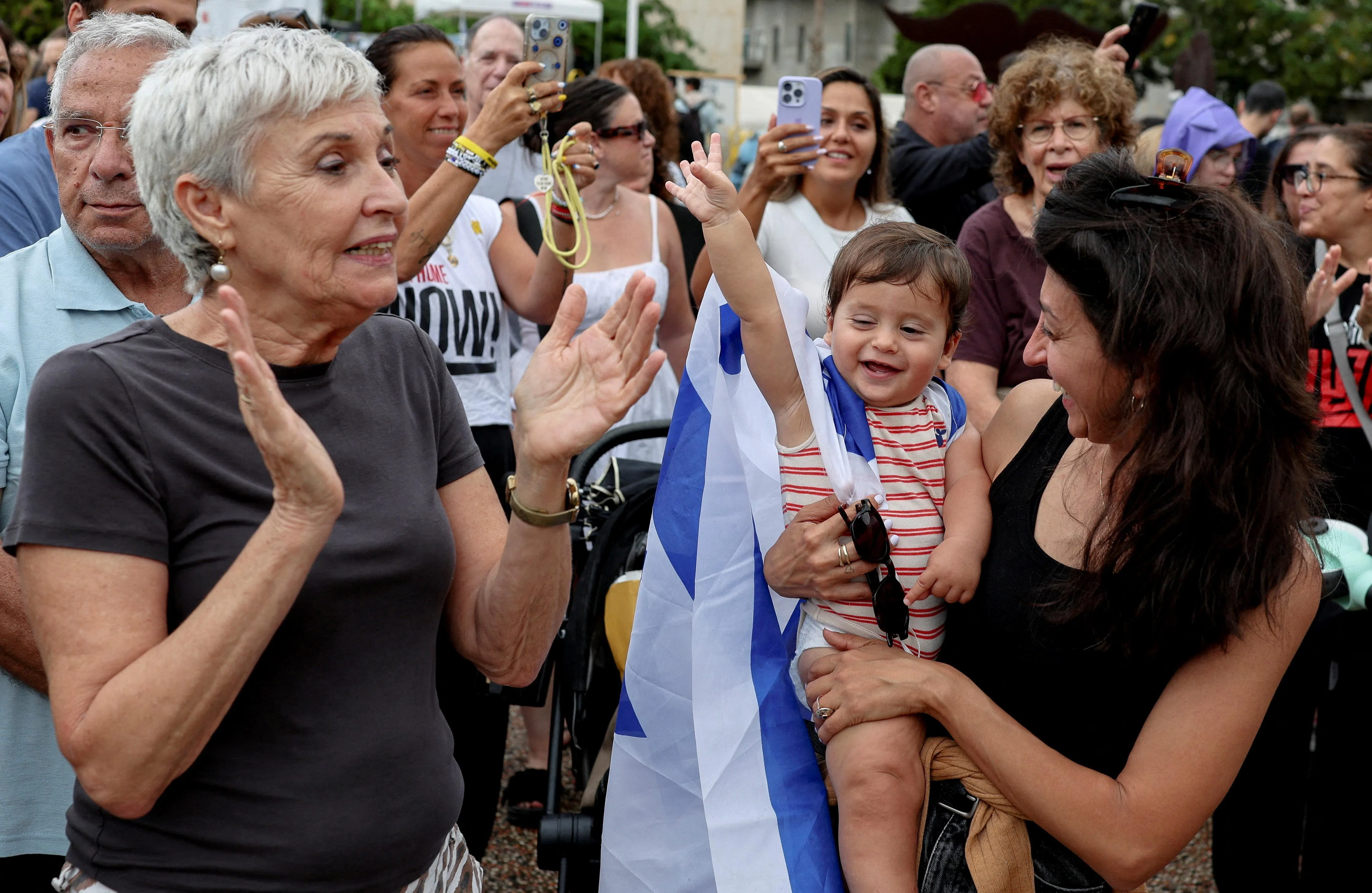 10月9日，人们聚集在特拉维夫“人质广场”庆祝停火，镜头前的孩子披着以​​色列国旗。（路透社）