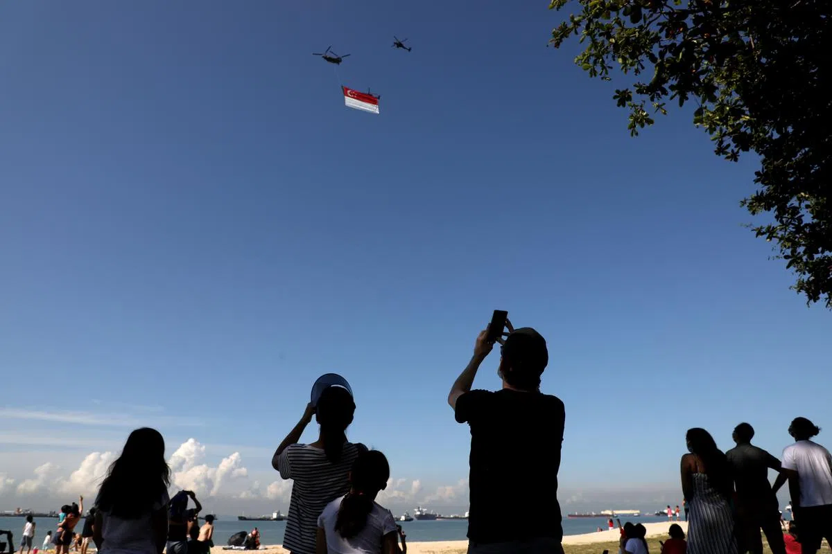 在东海岸公园度过假日的家庭看到大国旗飞过时，都急忙拿出手机拍照留念。（何炳耀摄）