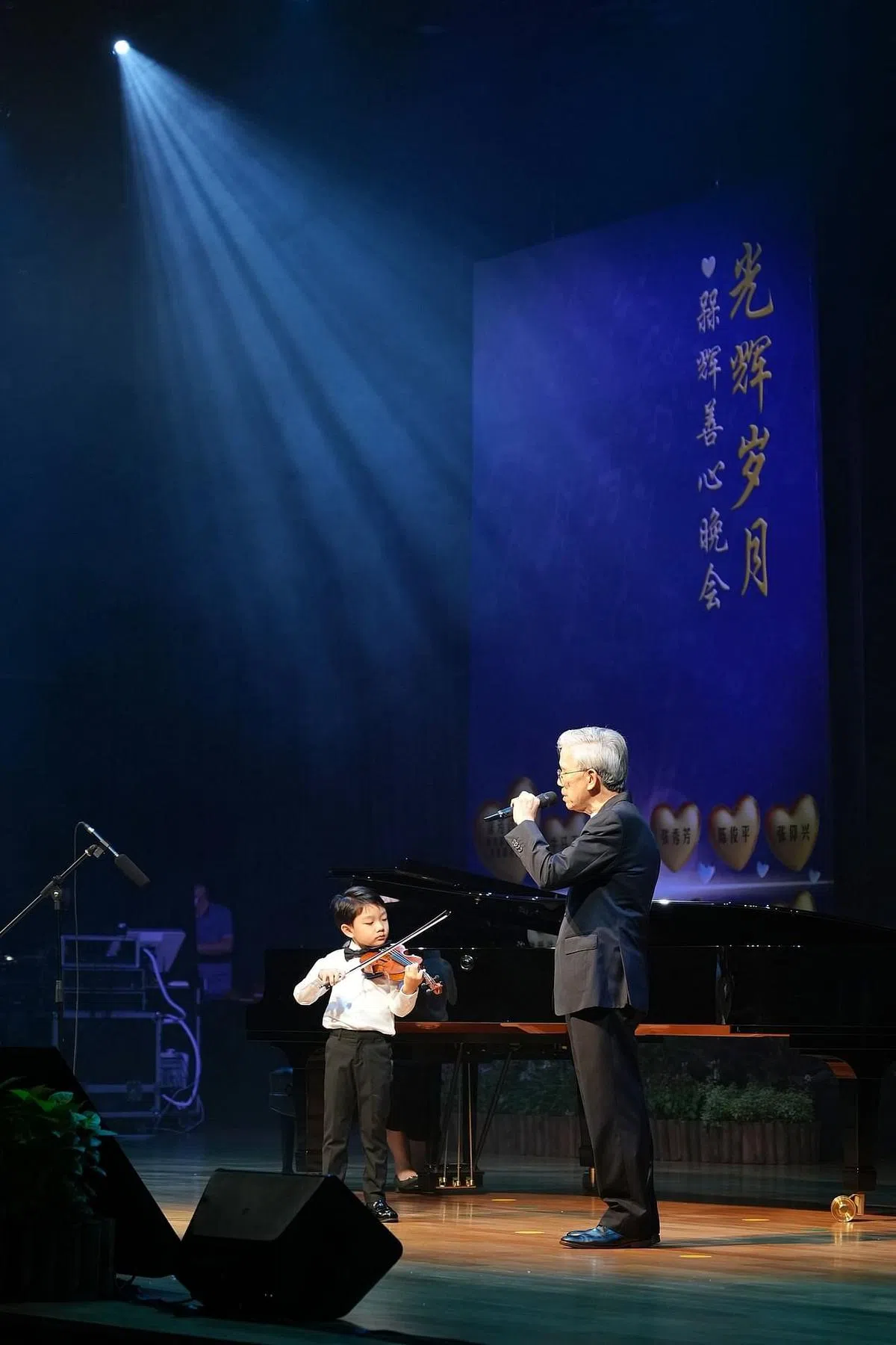 胡财辉（右）首次挑战英文歌，6岁的孙子胡宸玮用行动支持爷爷，以小提琴伴奏，祖孙首次同台演出。曾任育能小学校长的林素珠也以钢琴伴奏。（谢智扬摄）