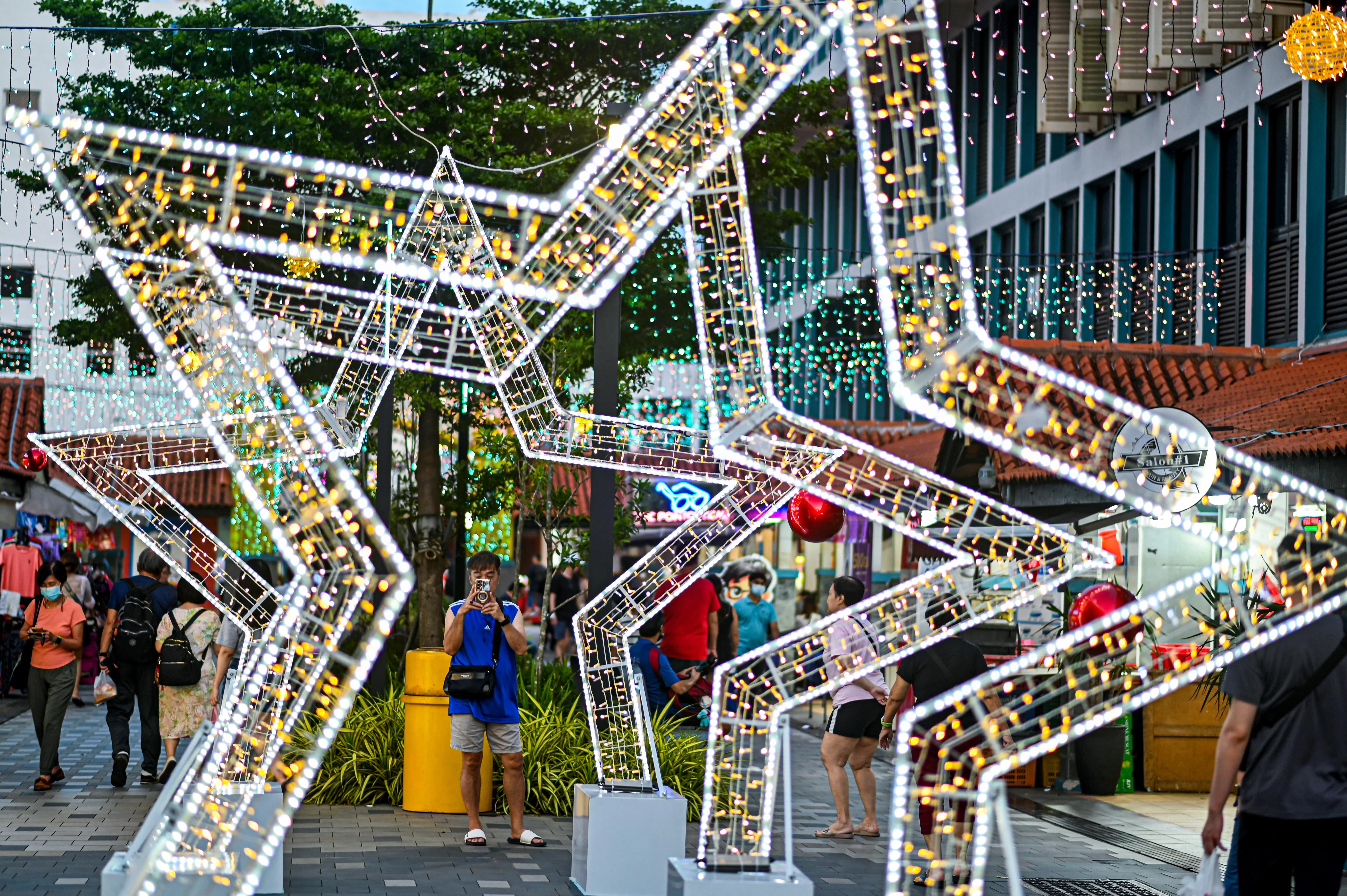 大巴窑中心两排店屋中间的圣诞装饰以星星造型的拱门为主，闪烁的灯饰点亮街道，吸引路过的民众驻足拍照，为热闹的街区增添浓厚的节日氛围。（李冠卫摄）
